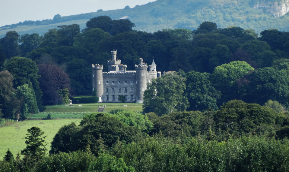 Gothic-style Tullynally Castle with battlements and towers, nestled among trees at the foot of rolling Westmeath hills.