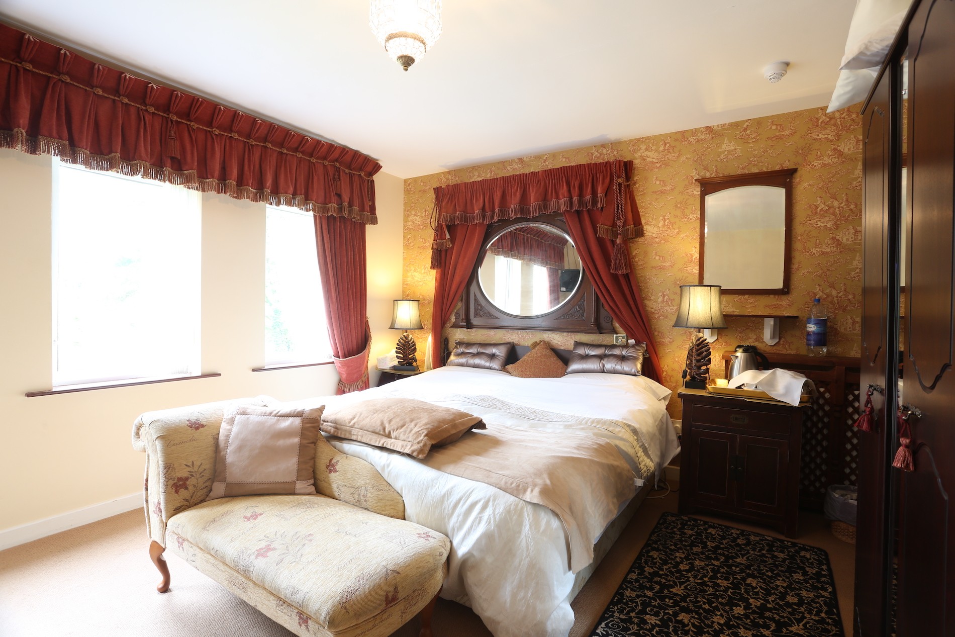 Chambre lumineuse à Arch House, comté de Fermanagh, avec mobilier de style vintage, lit à baldaquin, tapisserie florale et rideaux rouges.