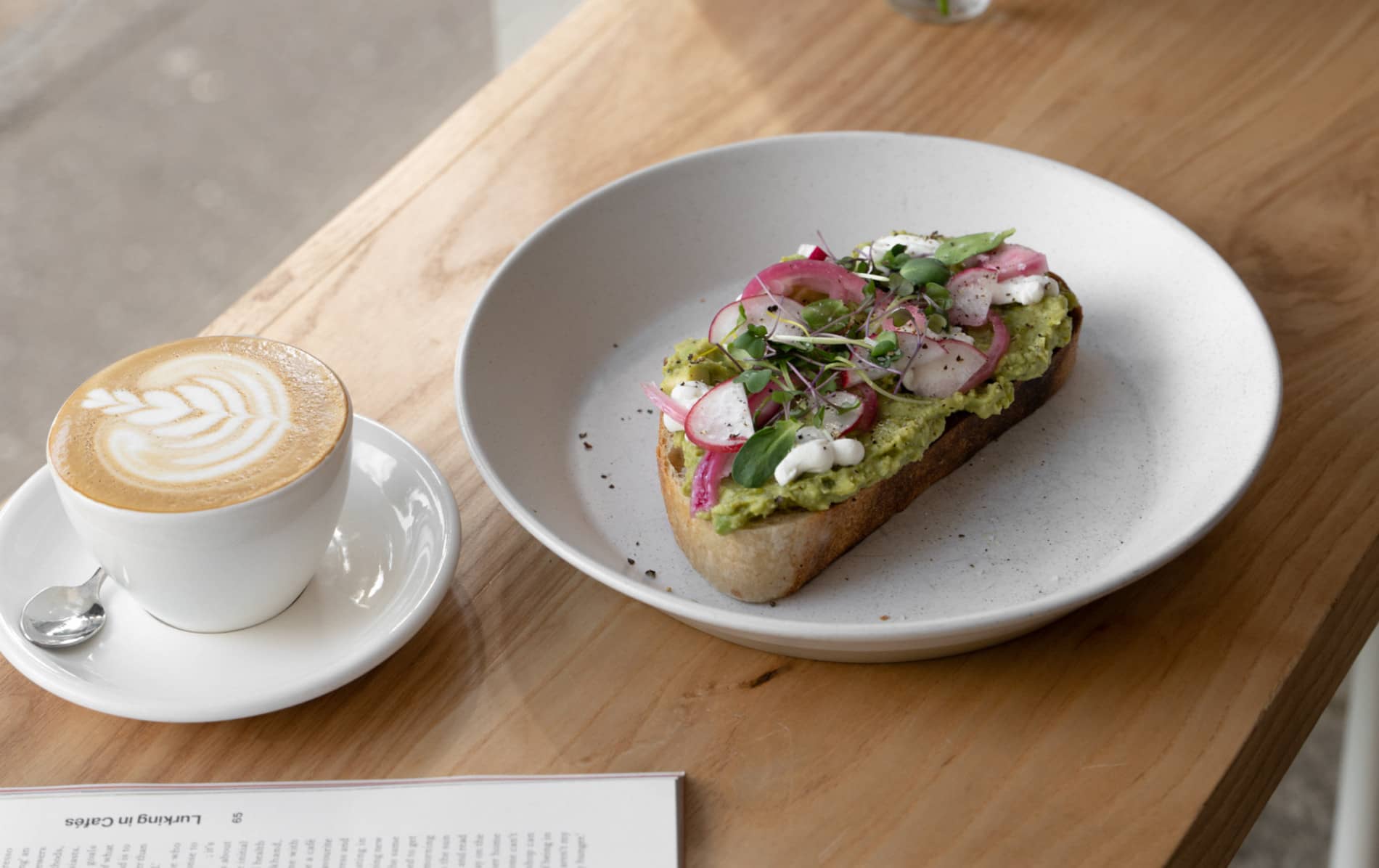 Avocado-Toast mit eingelegter Zwiebel und Kräutern, serviert mit einem Latte im Neighbourhood Café in Belfast.