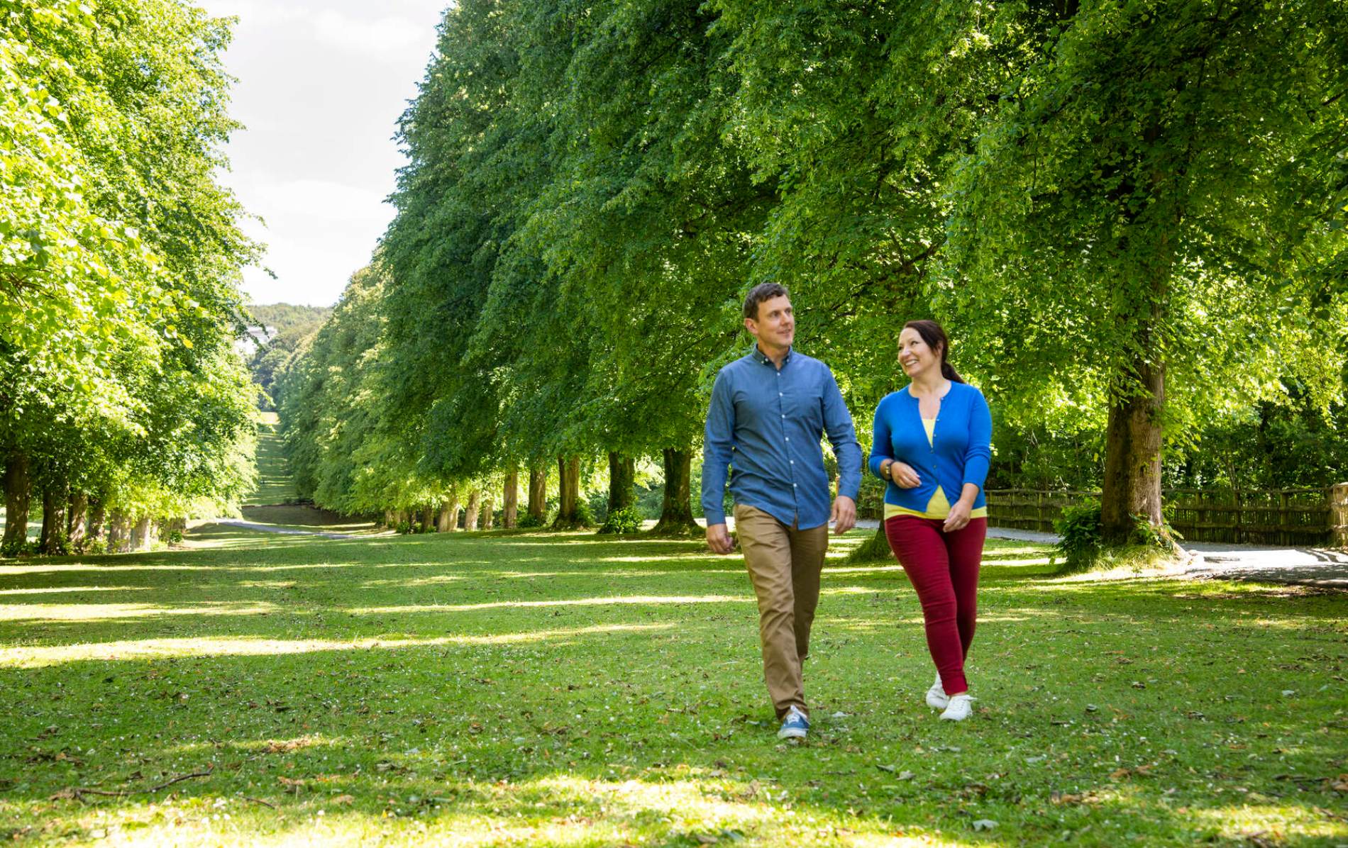 Couple walking under a canopy of trees in Stormont Estate, Belfast.
