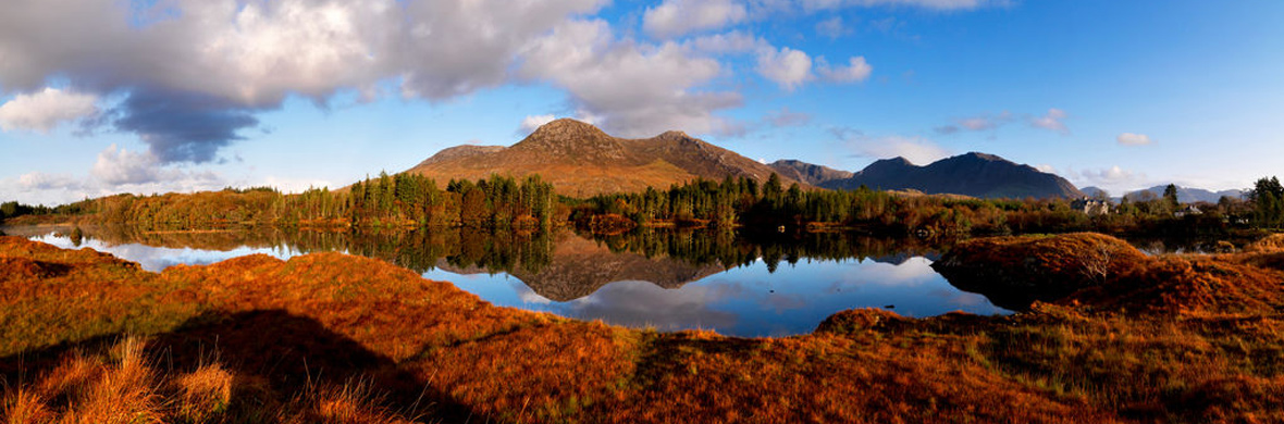 Herfstkleuren weerspiegelen in een meer aan de voet van de Twelve Bens bergen in Connemara, county Galway.