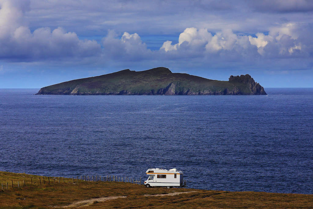 A motorhome parked on a clifftop in Dingle, Kerry, facing the Atlantic Ocean with views of a dramatic island offshore.