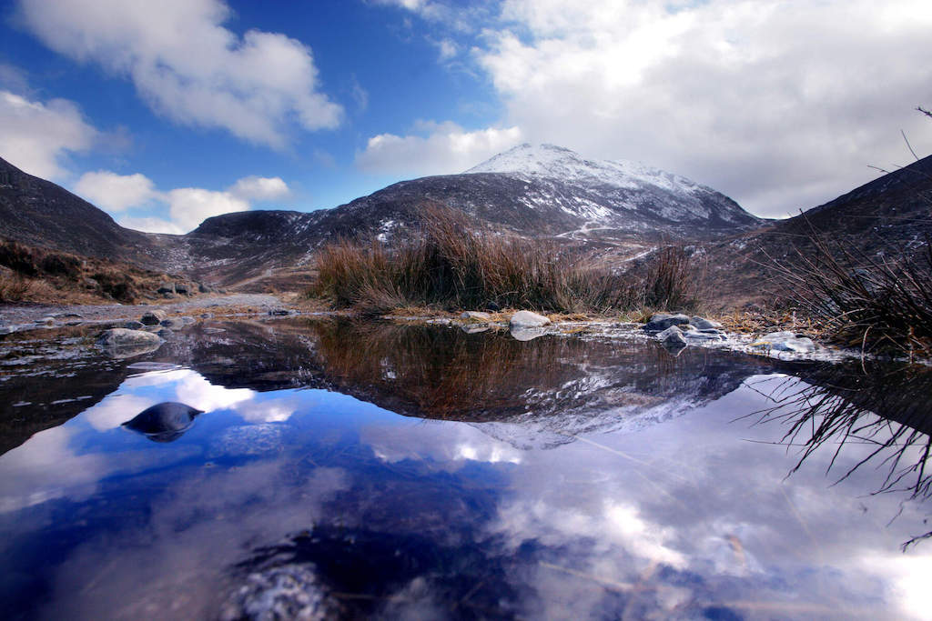 Snow-dusted peak in the Mourne Mountains, County Down, reflected in a small pond surrounded by reeds.