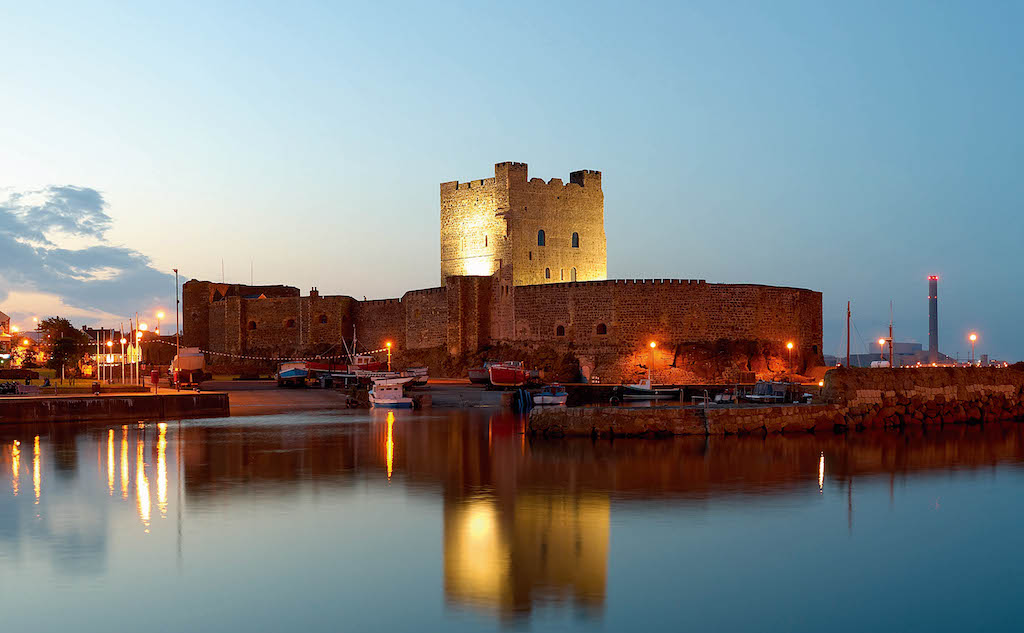 Carrickfergus Castle illuminated at dusk beside the harbour in County Antrim.