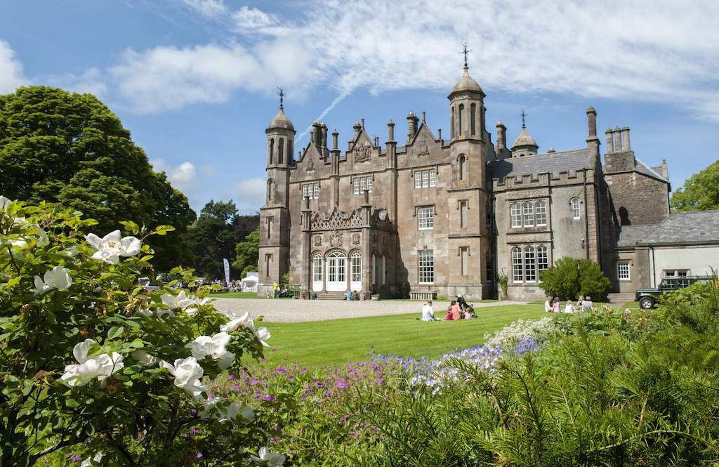 Gothic-style Glenarm Castle, County Antrim, with towers and chimneys surrounded by colourful gardens in summer bloom.