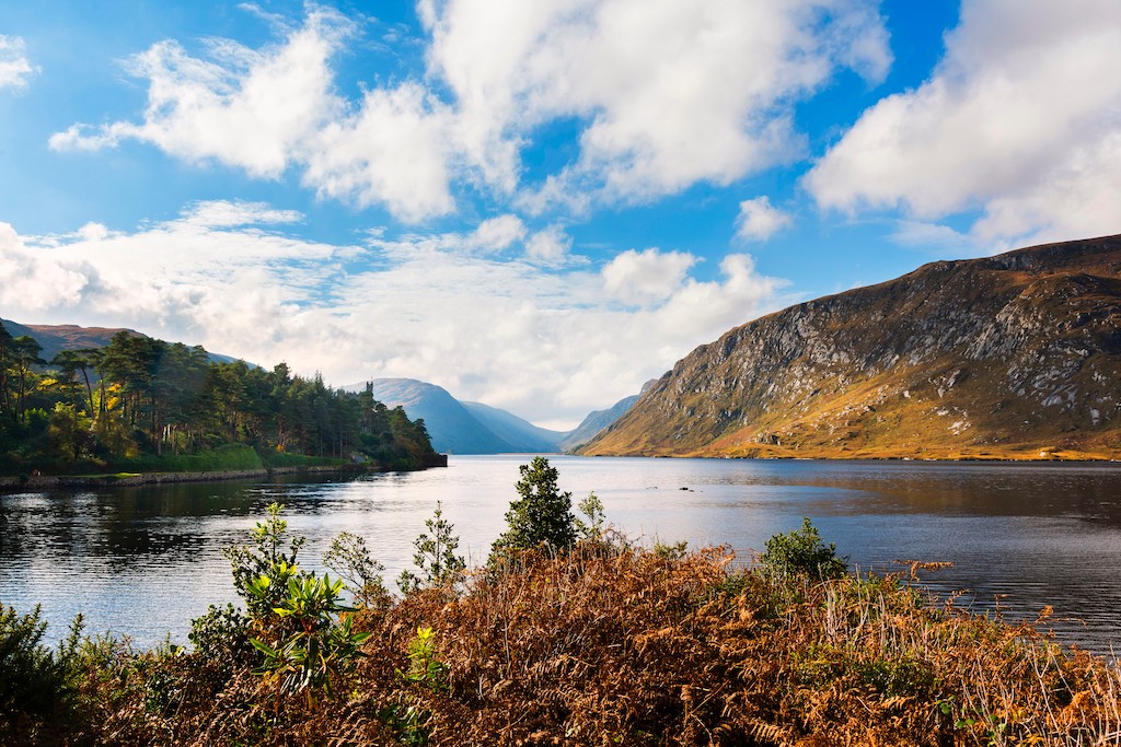 Glenveagh National Park lake with mountains and woodlands under a bright sky in County Donegal.