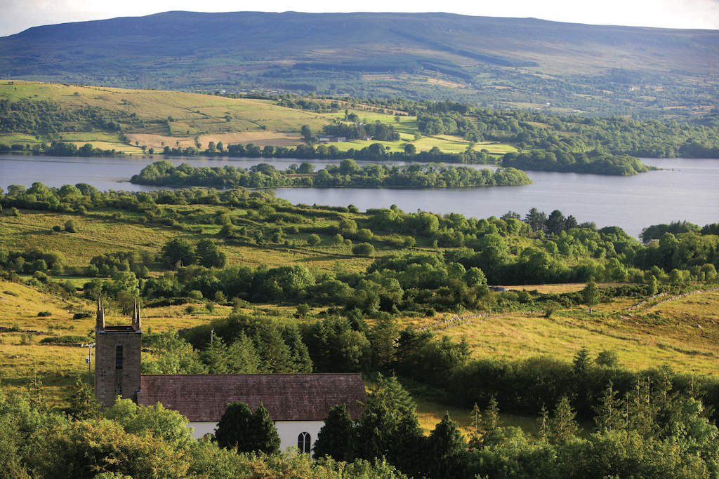 Green countryside landscape with a lake, patchwork fields and a church in Donegal.