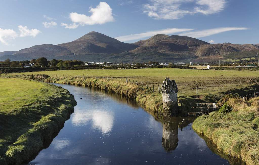 River reflecting blue sky and Mourne Mountains in the distance in County Down.