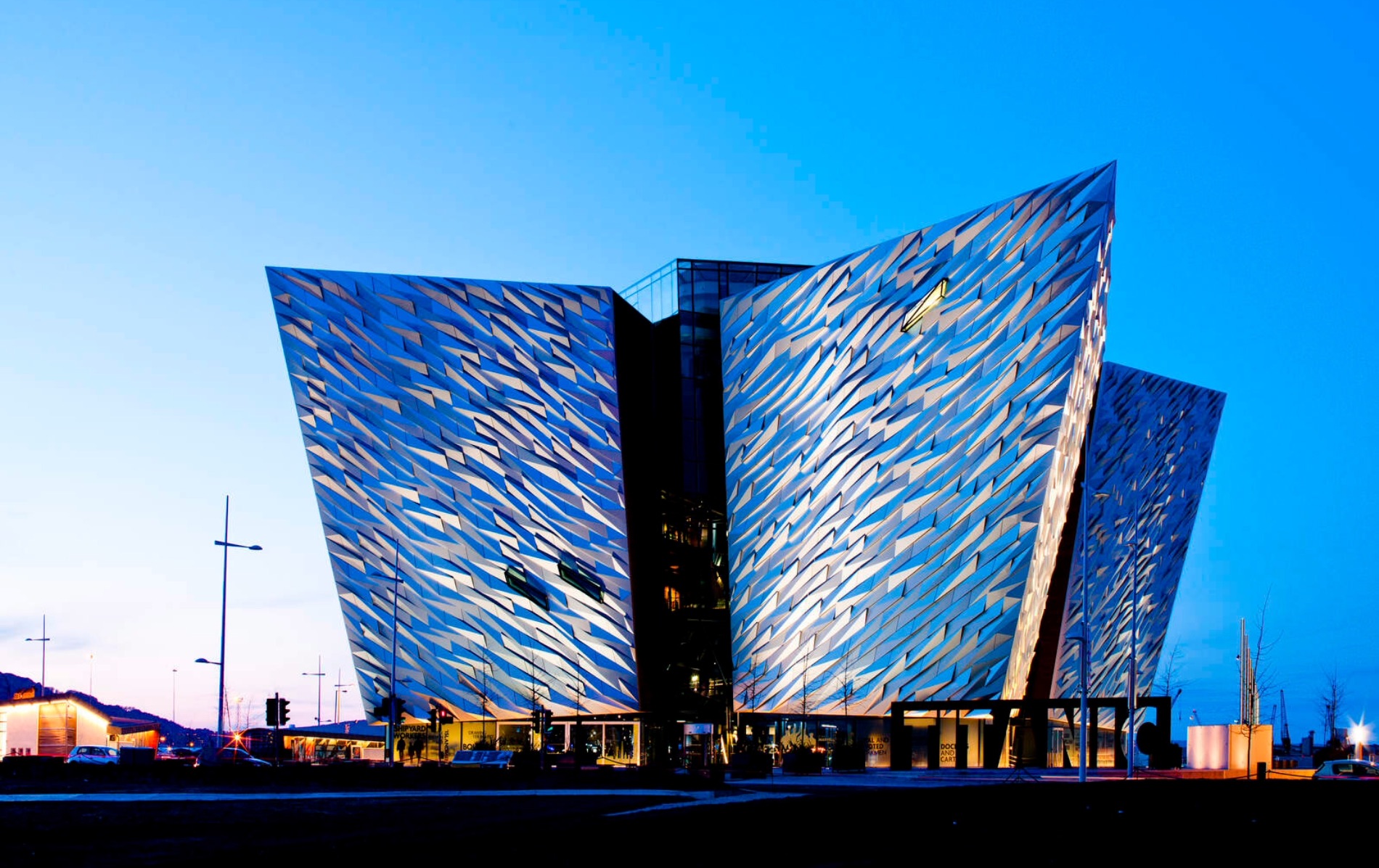 Avondzicht op het Titanic Belfast museum, met zijn hoekige gevel verlicht tegen een diepblauwe lucht in het Titanic Quarter.