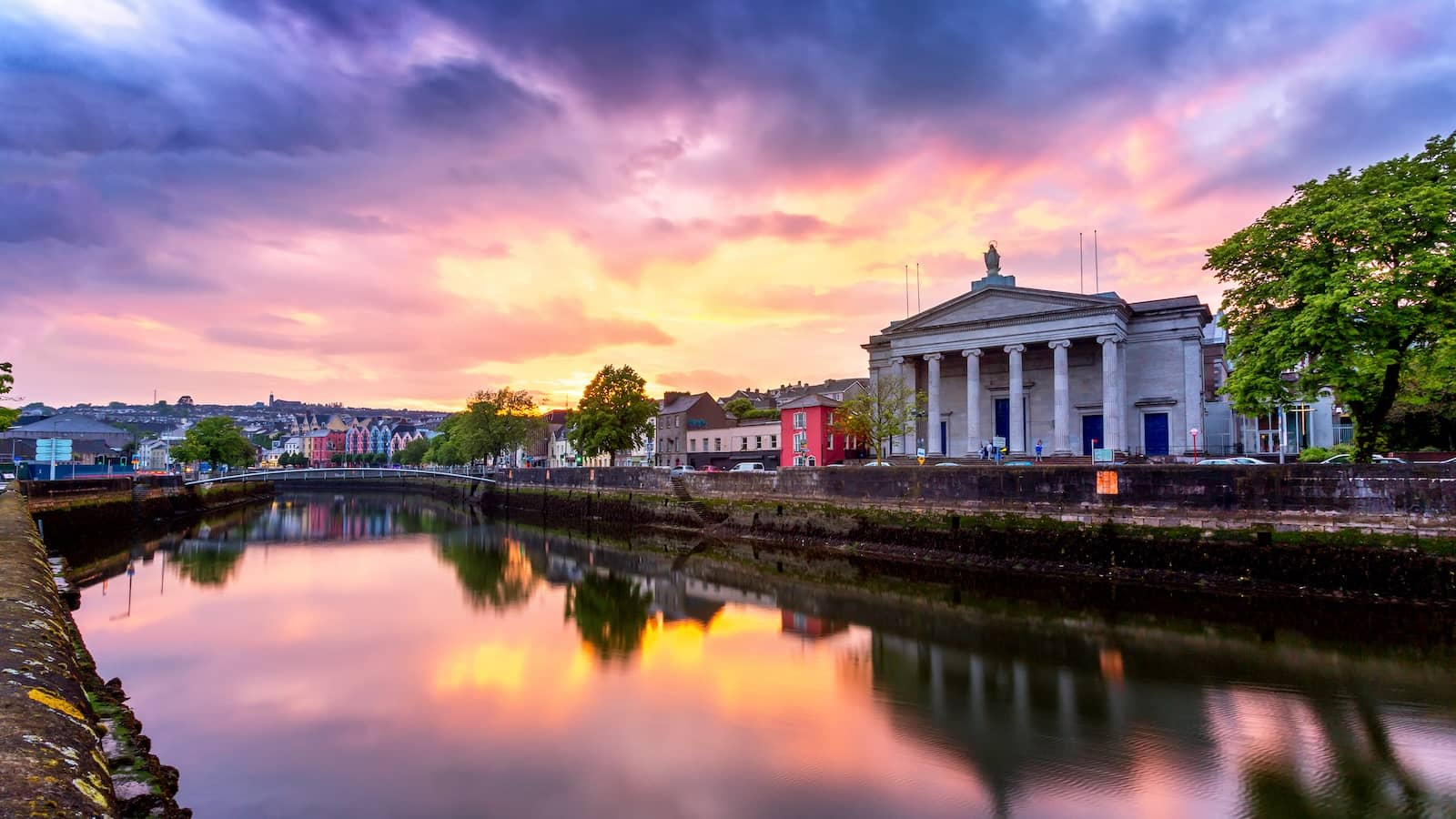 Cork Courthouse and River Lee at sunset, Cork City, with colourful sky reflected on calm water.