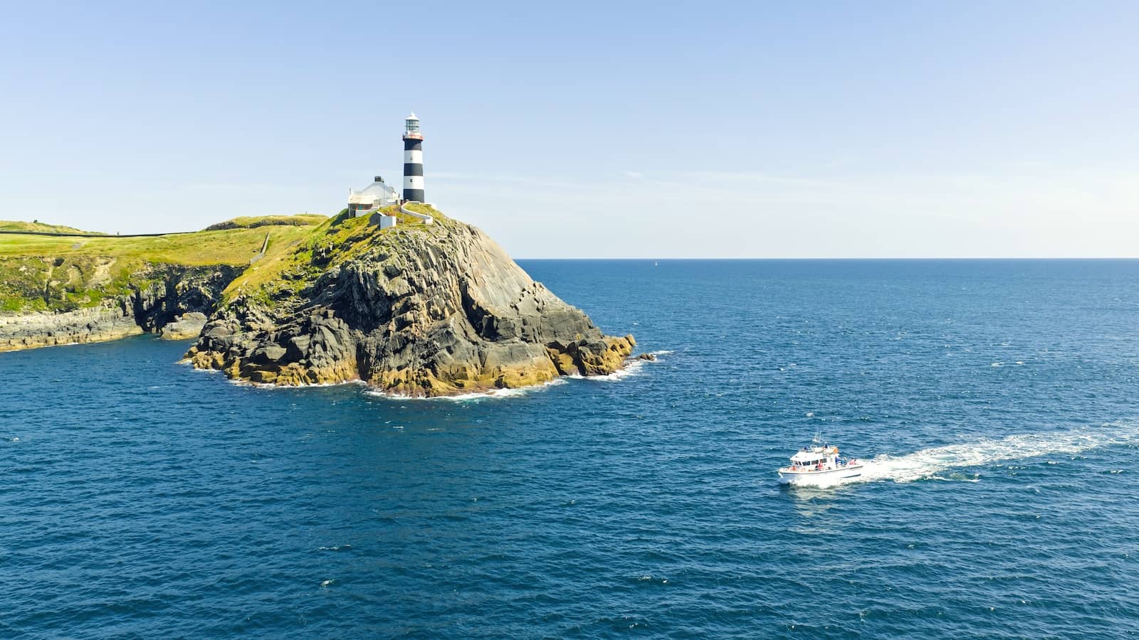 Old Head of Kinsale lighthouse, County Cork, on rugged cliffs above the Atlantic Ocean with passing boat.