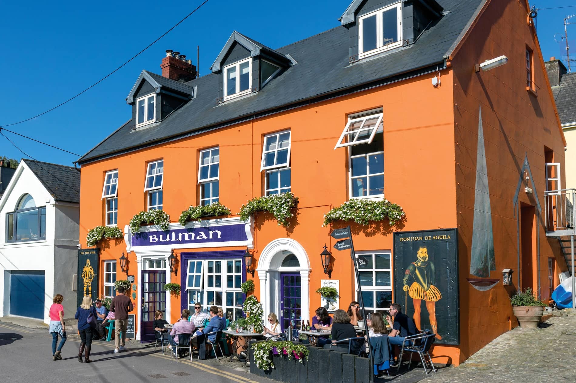 The Bulman pub exterior in Kinsale, County Cork, with bright orange façade and outdoor dining on sunny street.