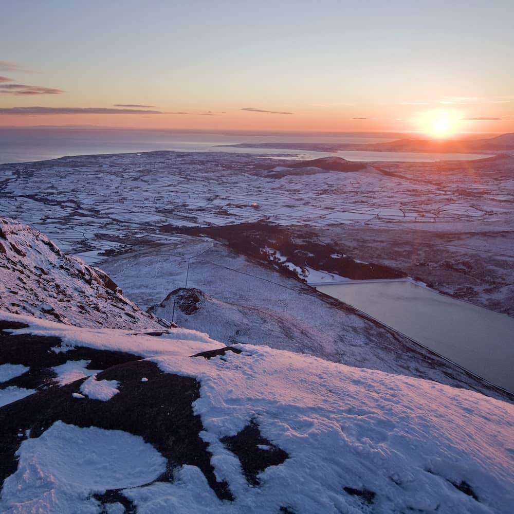 Die schneebedeckten Mourne Mountains bei Sonnenaufgang mit Blick auf die hügelige Landschaft, Seen und die Küste in der Nähe von Newry.