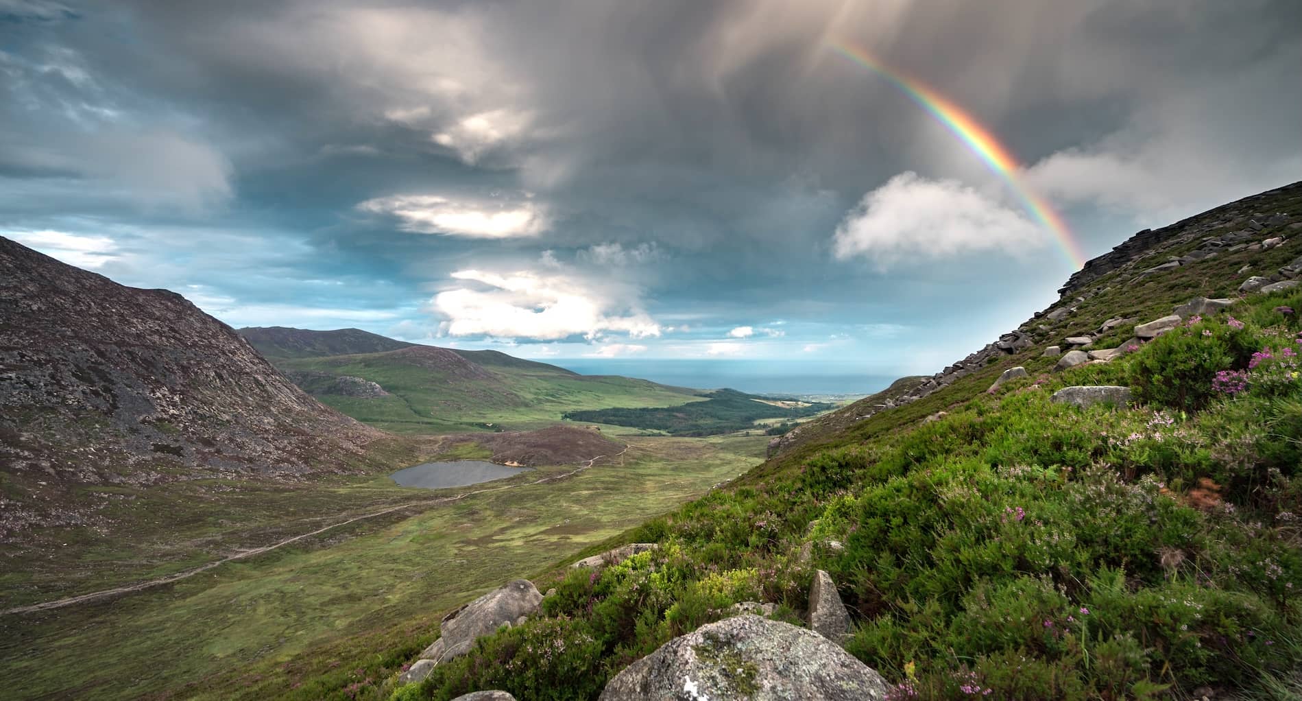 Rainbow over the Mourne Mountains with sweeping valley views, rocky hillsides and dramatic skies in County Down.