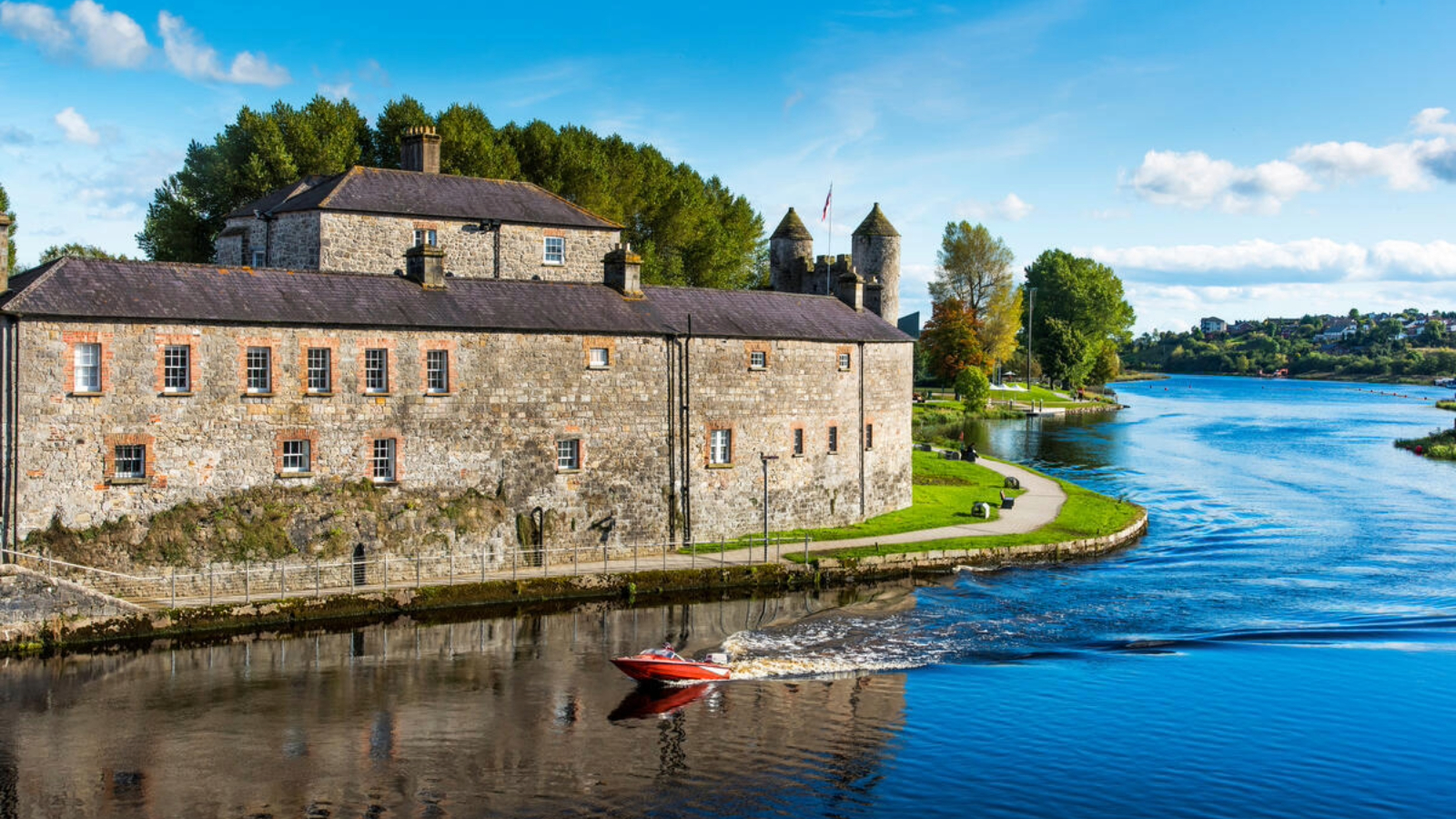 Enniskillen Castle beside the River Erne as a red motorboat passes on a bright sunny day.