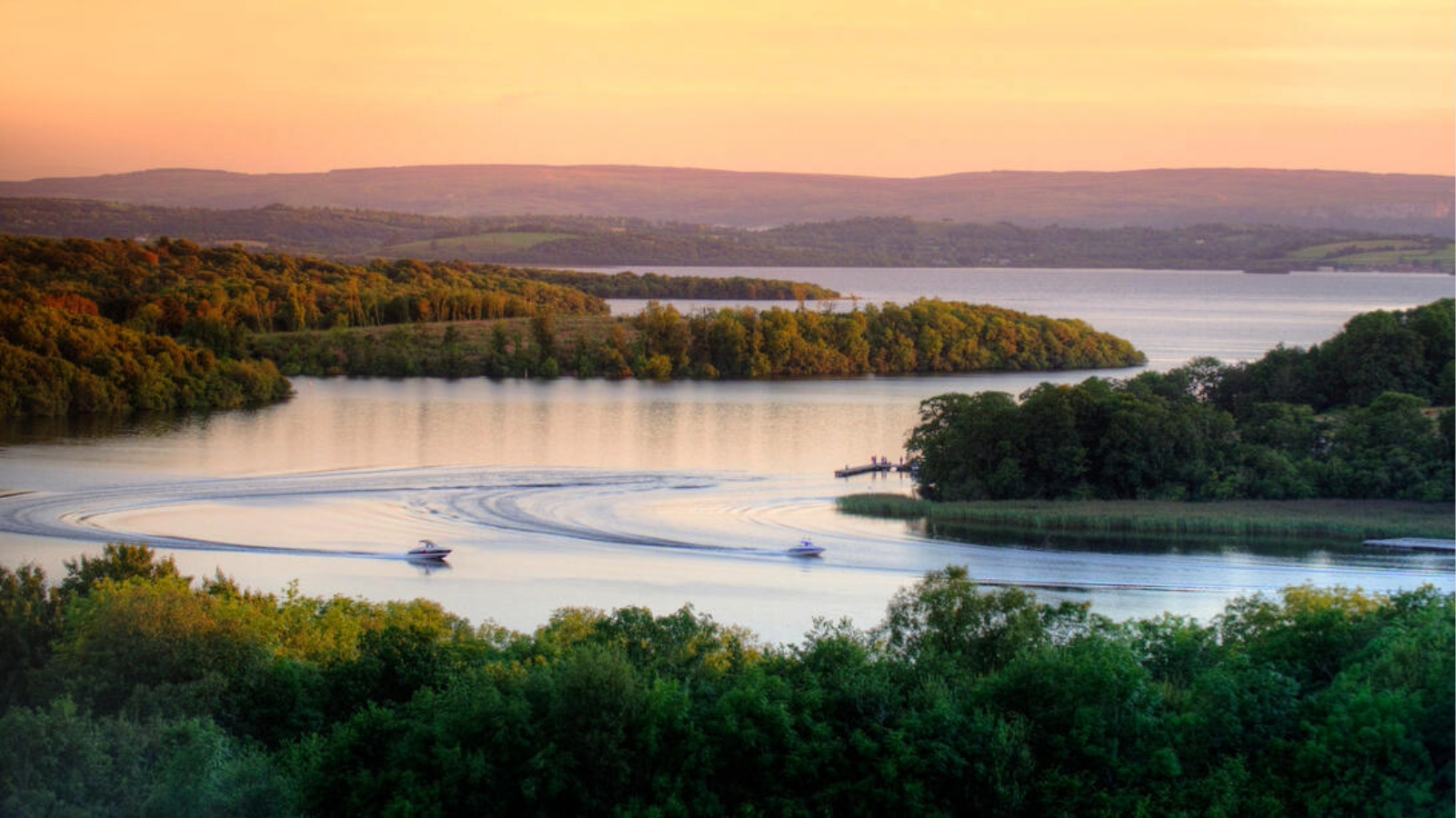 Motorboats leave curved wakes across the Fermanagh Lakelands at sunset in County Fermanagh.