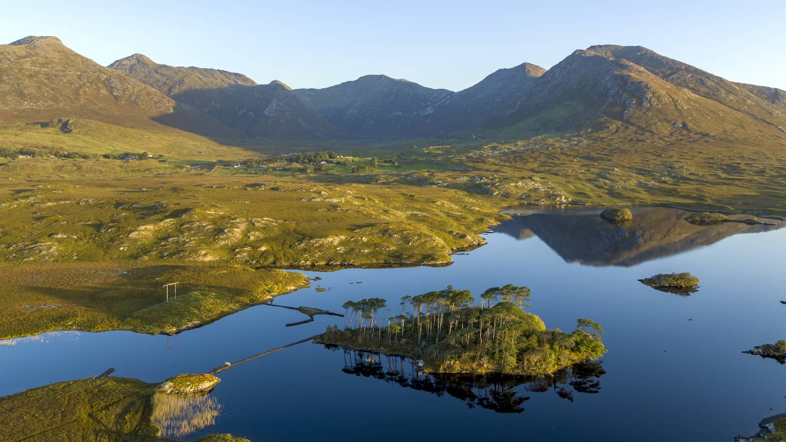 Lac Derryclare Lough dans le Connemara, dans le comté de Galway, avec petite île boisée, montagnes et reflets dans une eau calme.