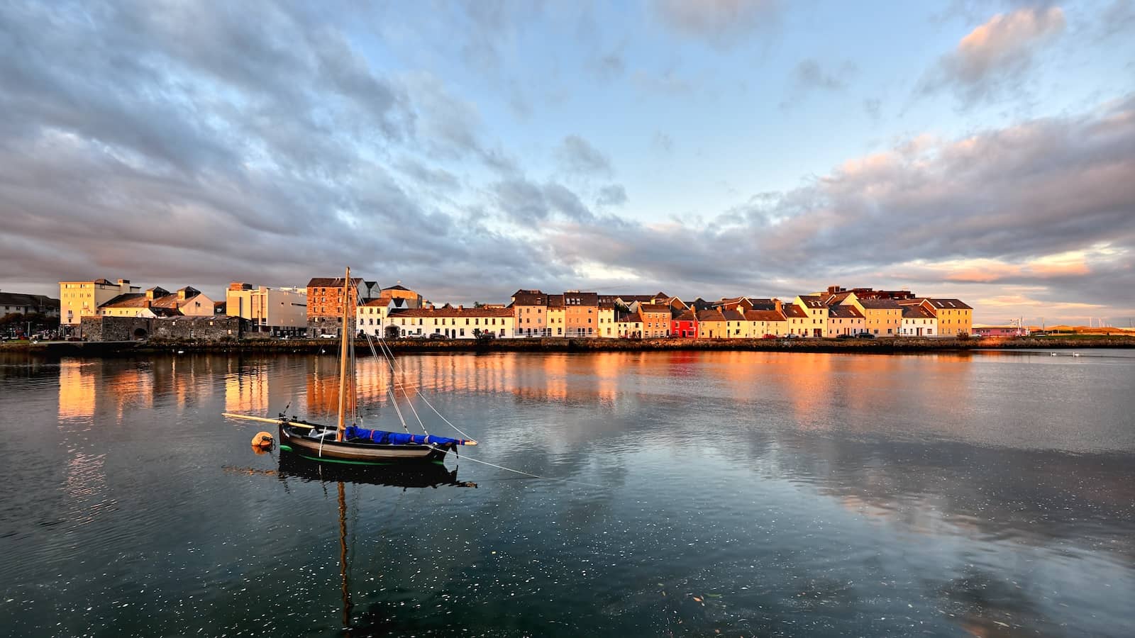 Long Walk et quartier du Claddagh à Galway au coucher du soleil, avec reflets de maisons colorées dans une eau calme.