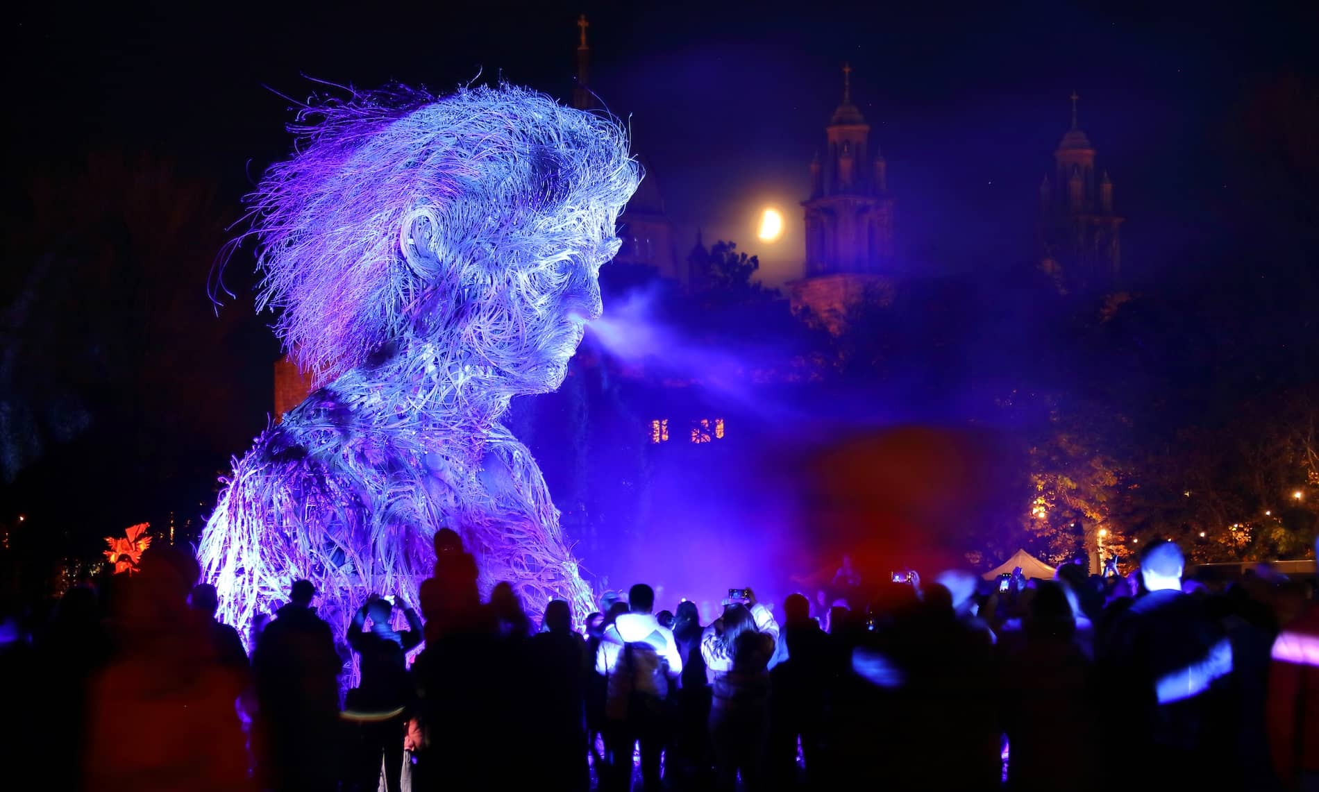 Crowds gathered around a glowing Macnas parade figure during Galway International Arts Festival at night.