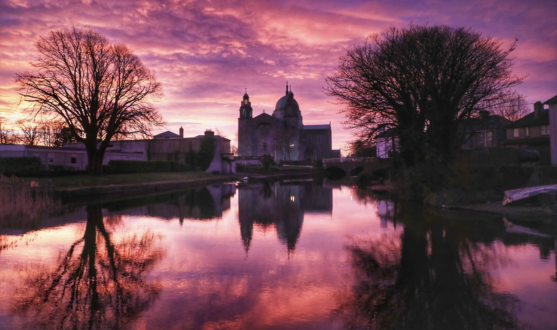 Galway Cathedral riflessa nell'acqua calma sotto un cielo viola al tramonto nella città di Galway.
