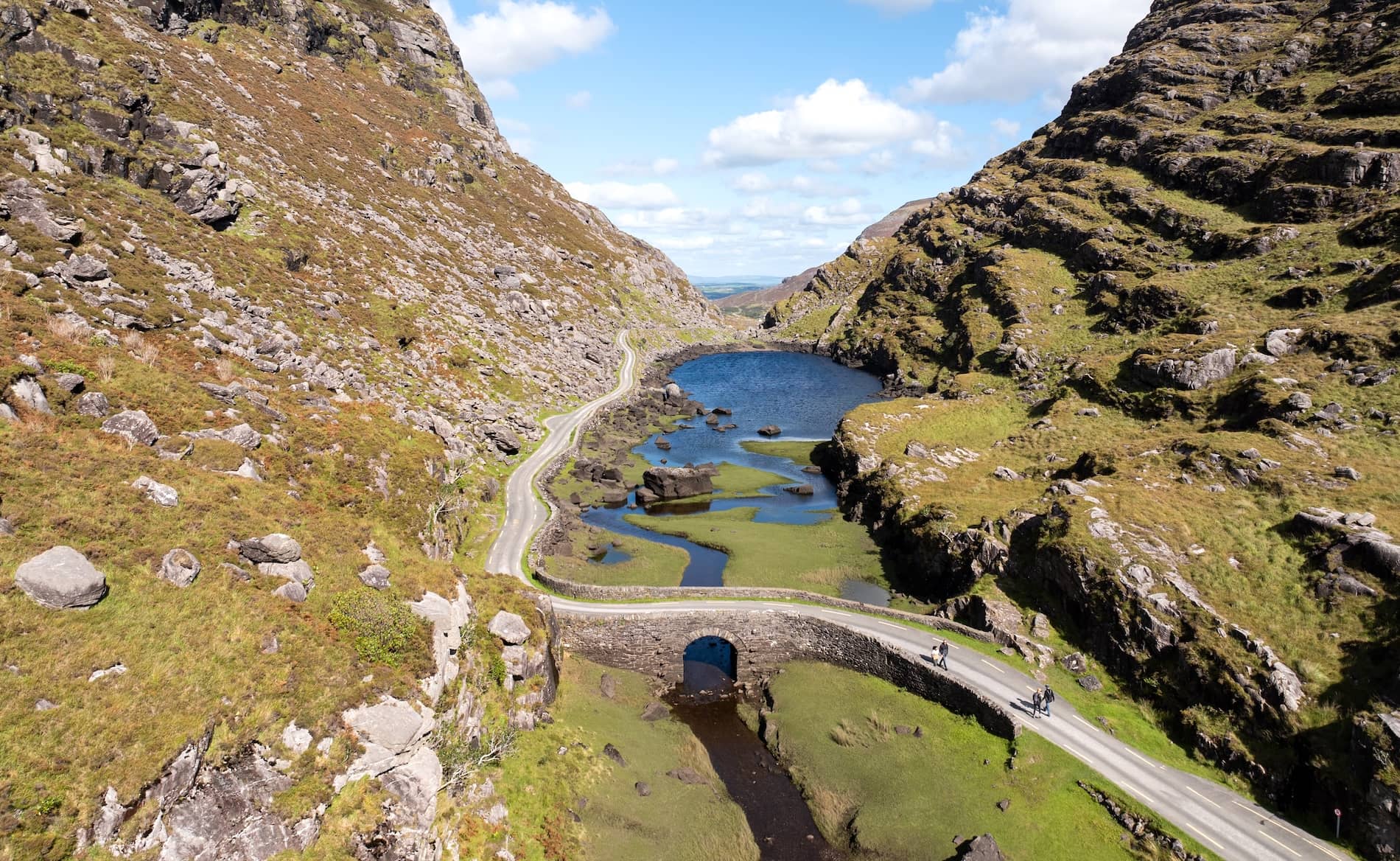 Aerial view of the Gap of Dunloe, with a winding road, stone bridge and mountain lake in County Kerry, Ireland.
