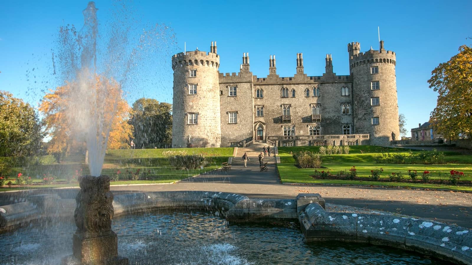 Château de Kilkenny se reflétant dans une fontaine, avec les jardins soignés et les tours historiques de la ville de Kilkenny.