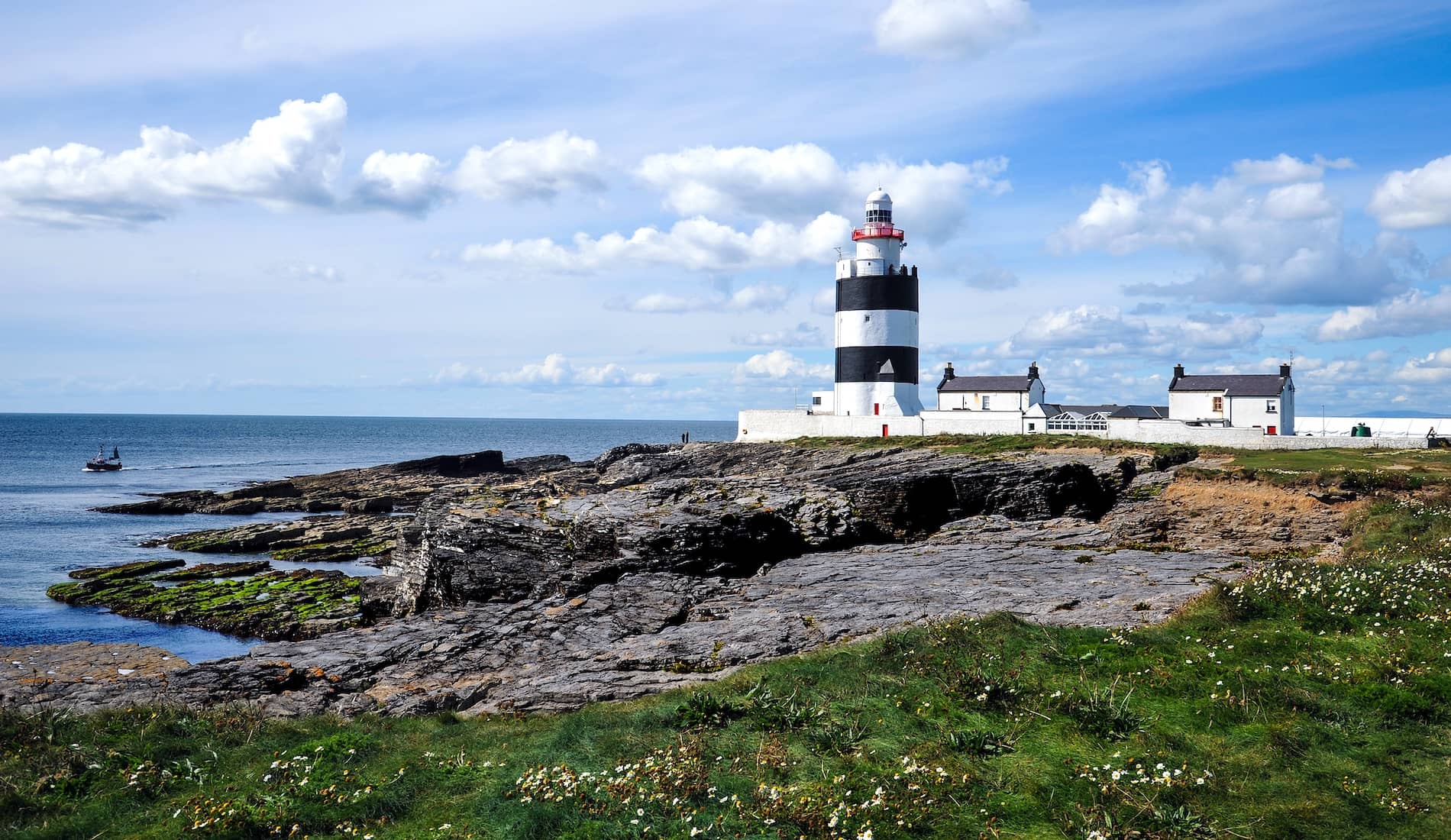 Hook Head Lighthouse in County Wexford, striped tower overlooking rocky coast and calm blue sea.