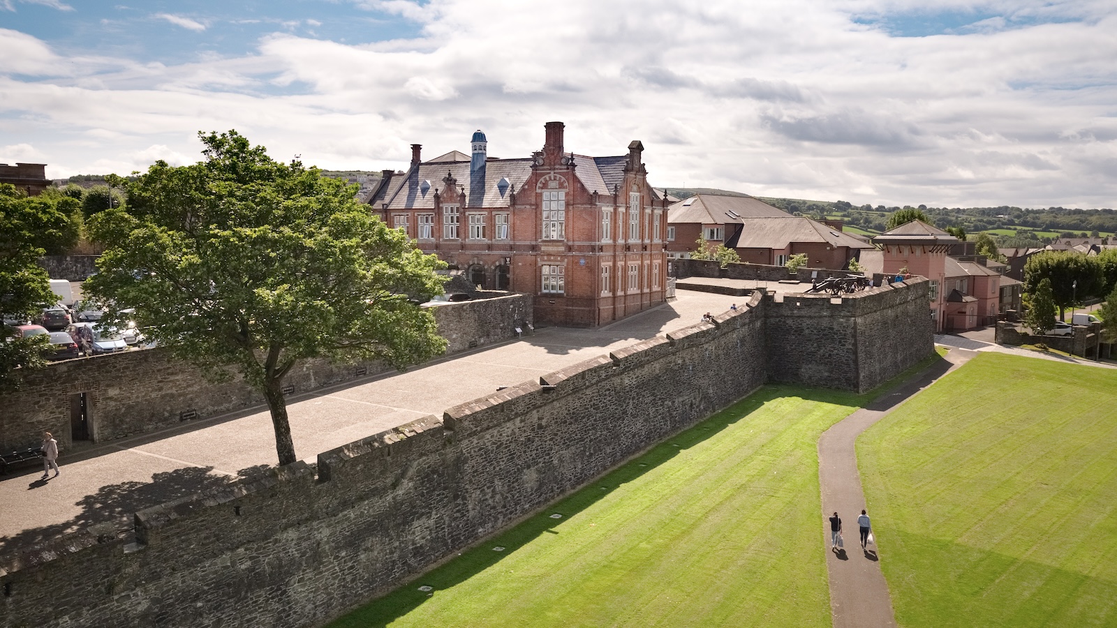 Menschen, die entlang der Stadtmauern von Derry~Londonderry spazieren, mit Grünflächen und historischen Gebäuden.