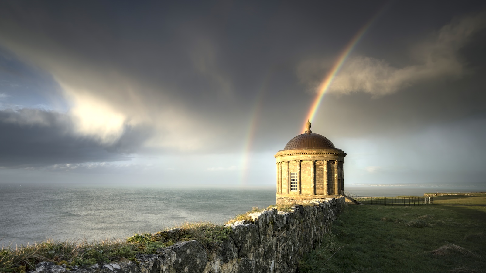 Mussenden Temple in der Grafschaft Londonderry, eingerahmt von einem doppelten Regenbogen über imposanten Küstenklippen.