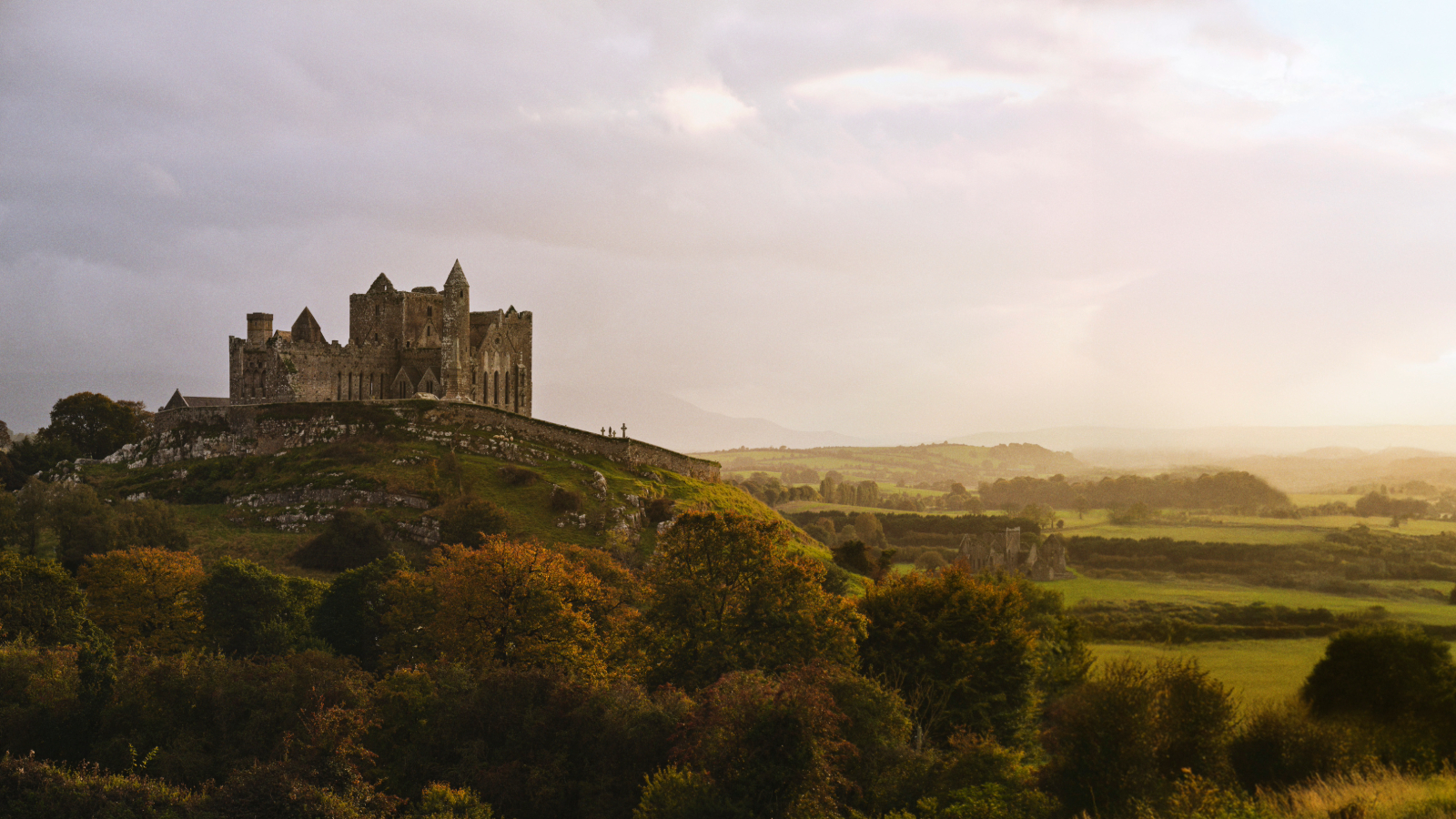 Rock of Cashel on a hill above County Tipperary countryside beneath dramatic sunbeams breaking through clouds.