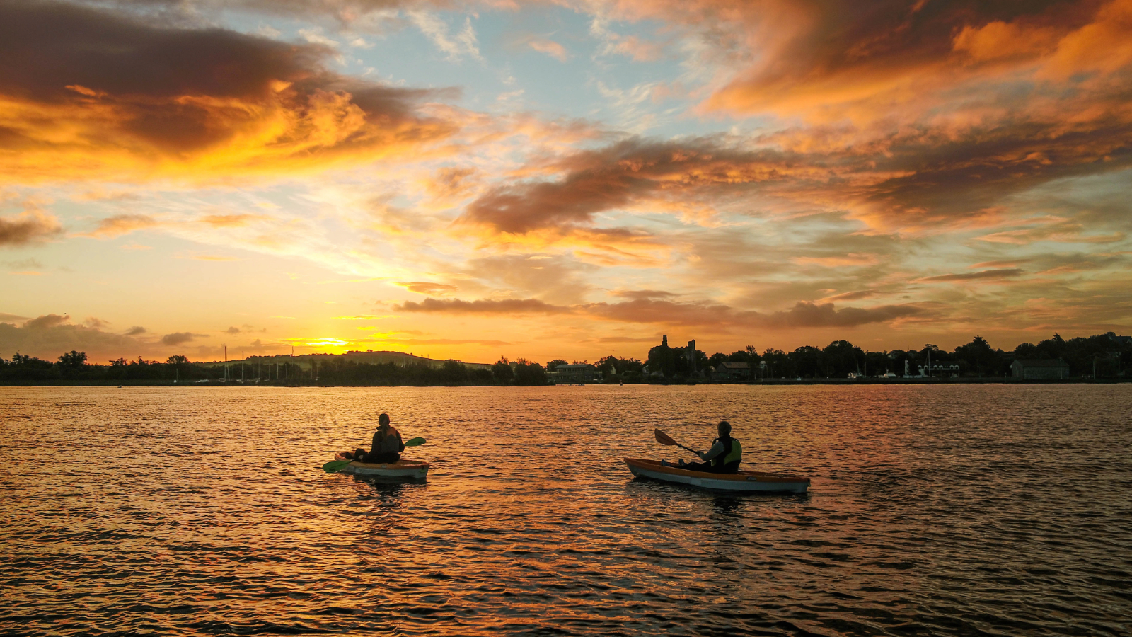 Two people kayaking on Lough Derg at sunset with warm skies reflected across the water, County Tipperary.