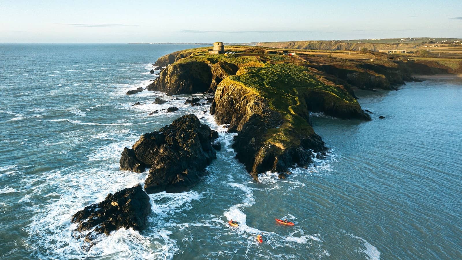 Baginbun Head cliffs with kayakers exploring the rugged coastline of County Wexford.