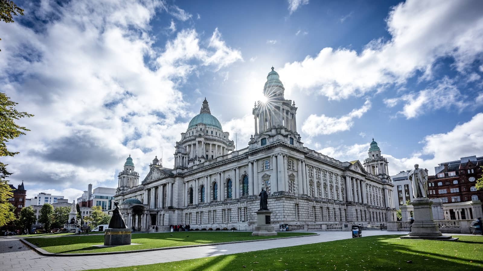 Belfast City Hall with its green domes and statues, lit by bright sunlight and blue skies.