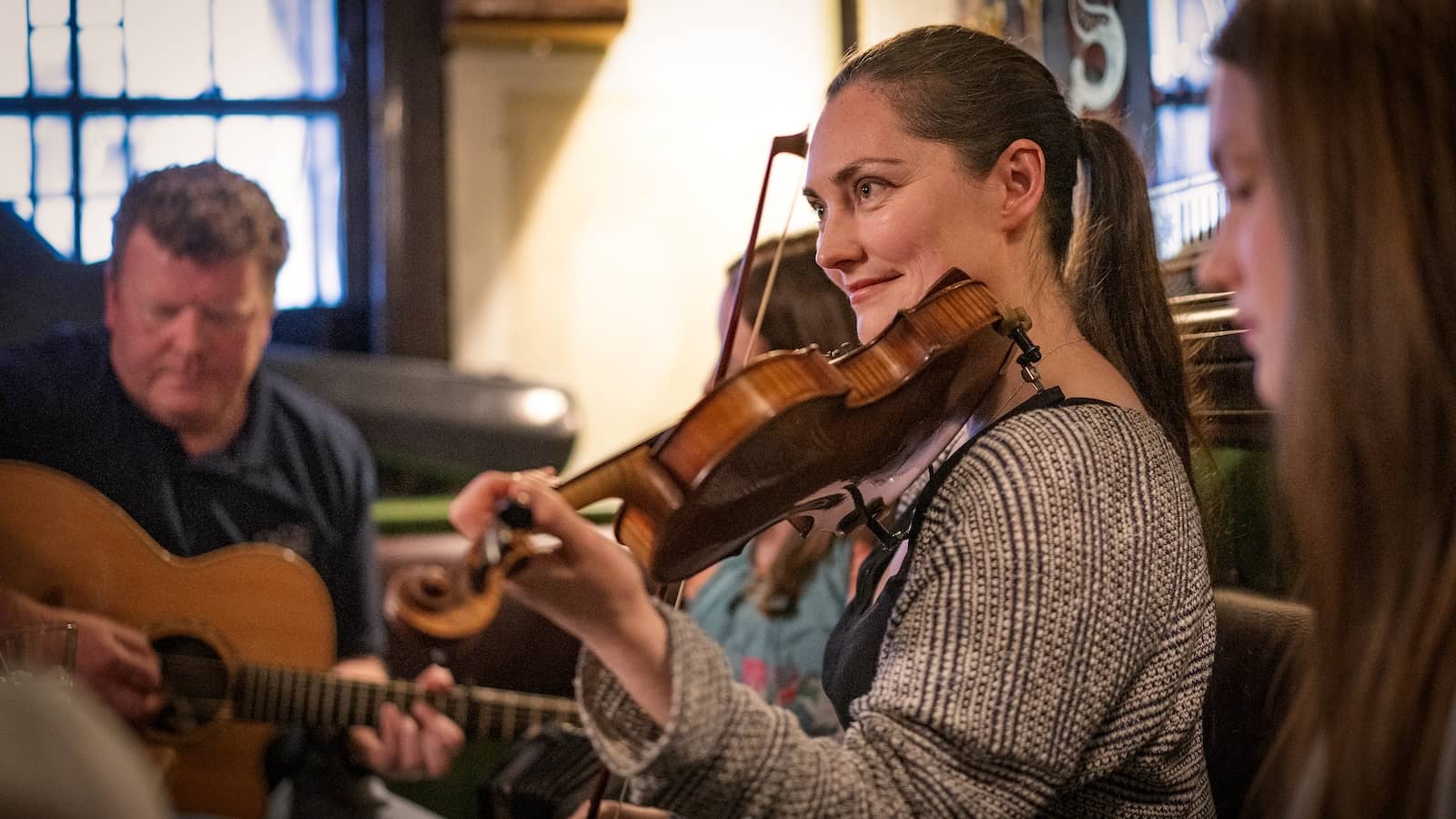 Een sessie met Traditionele Ierse muziek in een pub in Belfast, met een violist en gitarist die binnen spelen.