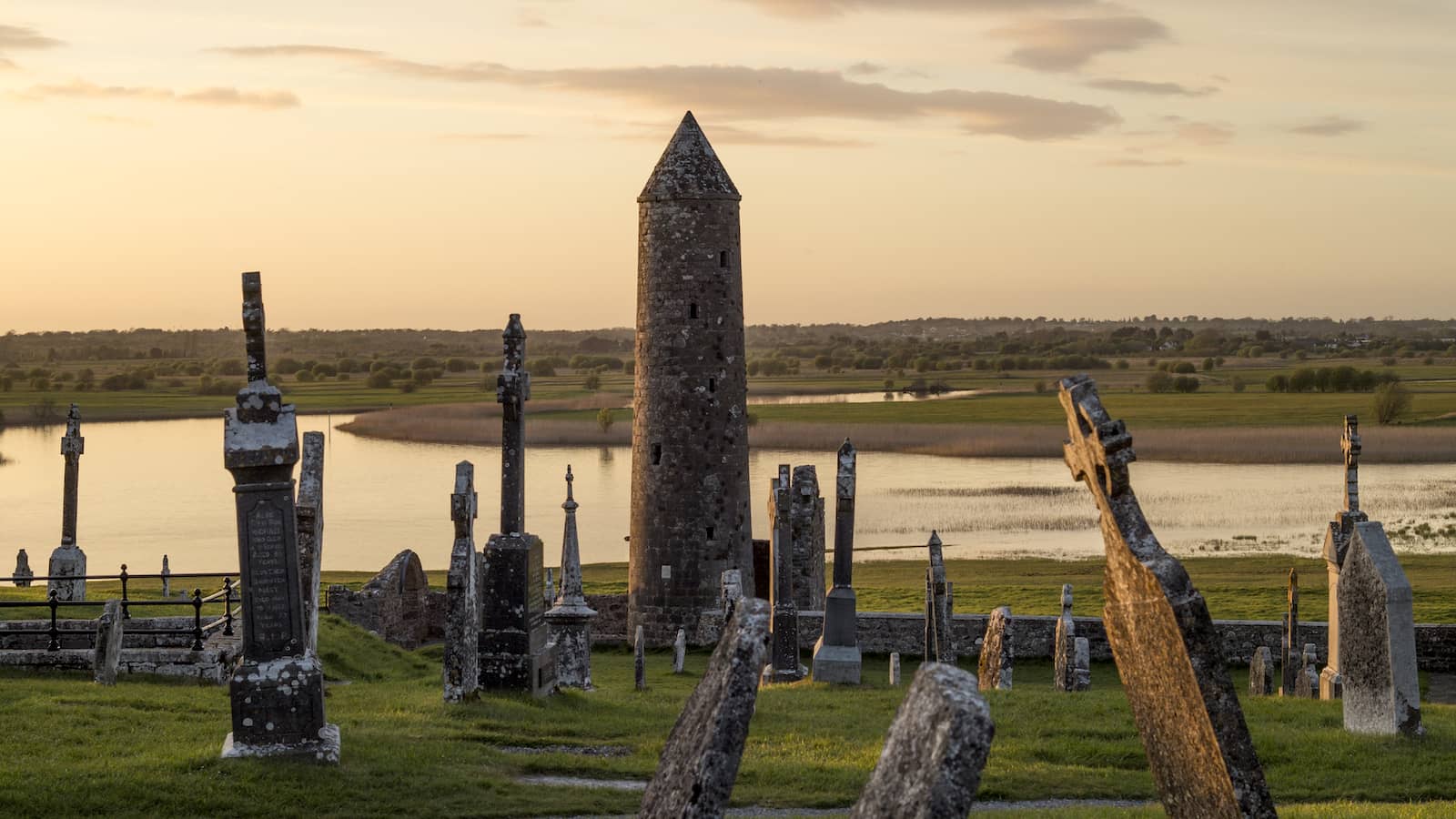 Clonmacnoise monastic site with round tower and gravestones overlooking the River Shannon at sunset in County Offaly.