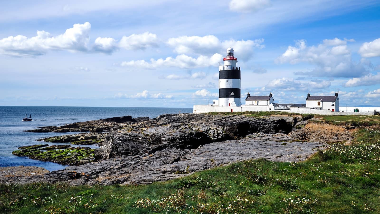 Das Hook Head Lighthouse an der Küste der Grafschaft Wexford steht auf felsigen Klippen neben weißen Cottages am Meer.