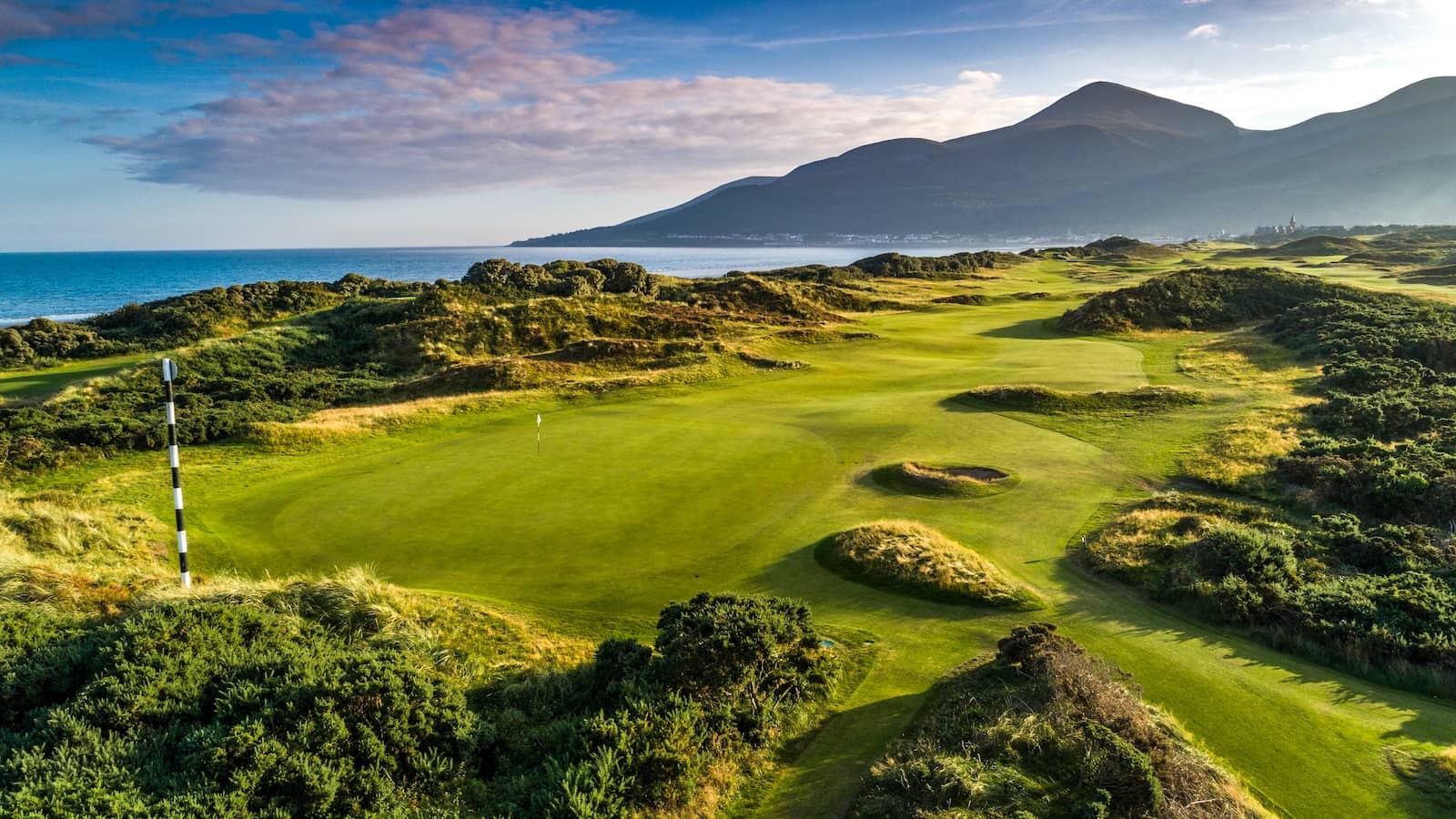 Lush fairways of Royal County Down golf course with sea views and the Mourne Mountains in the distance.