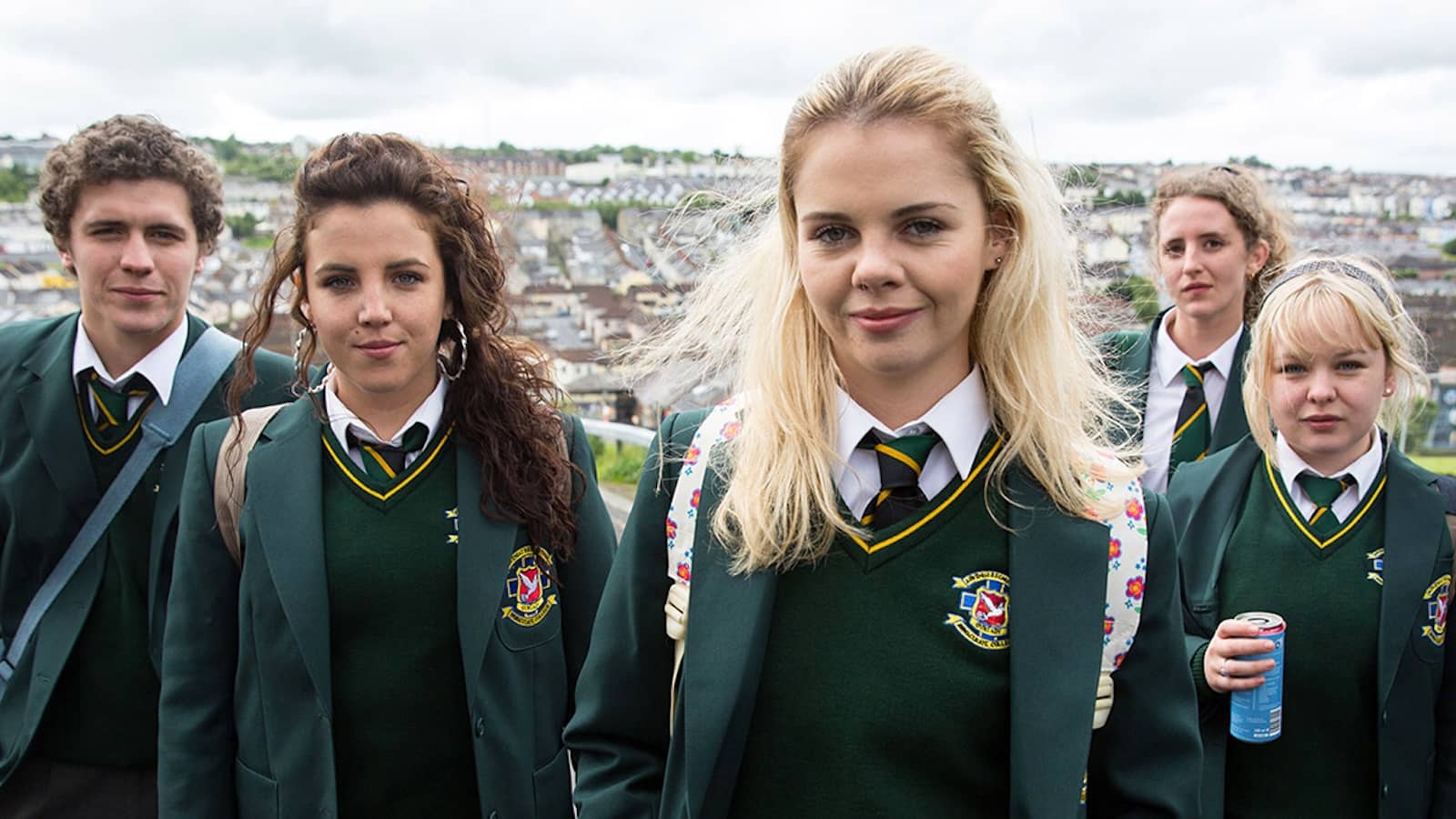 Group of teenagers in green school uniforms standing outdoors with a view of Derry~Londonderry in the background.