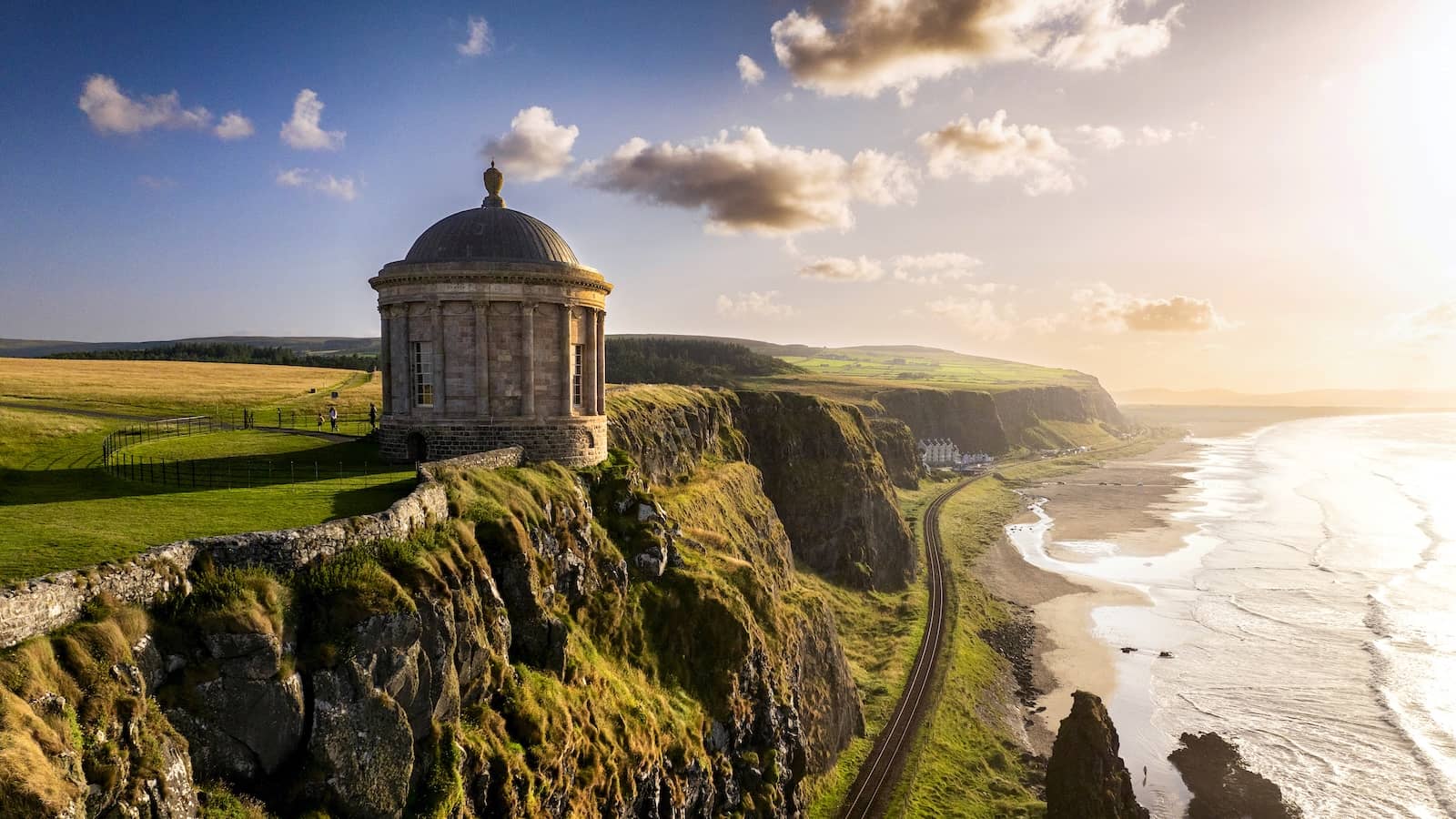 Mussenden Temple overlooking cliffside railway and coast at sunset in County Londonderry, Northern Ireland.