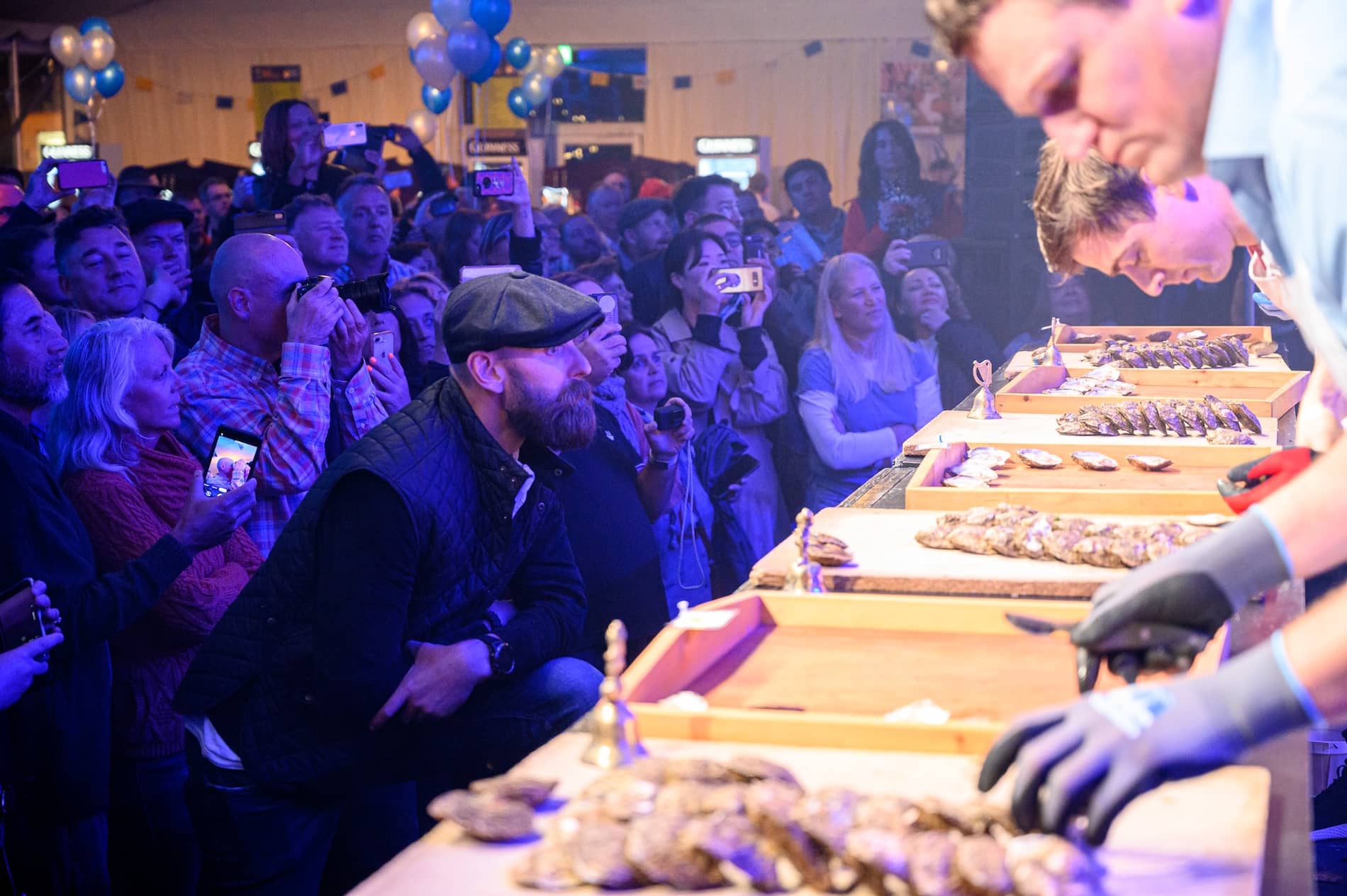 Close-up of oyster shuckers at work while a lively crowd watches at the Galway International Oyster Festival.