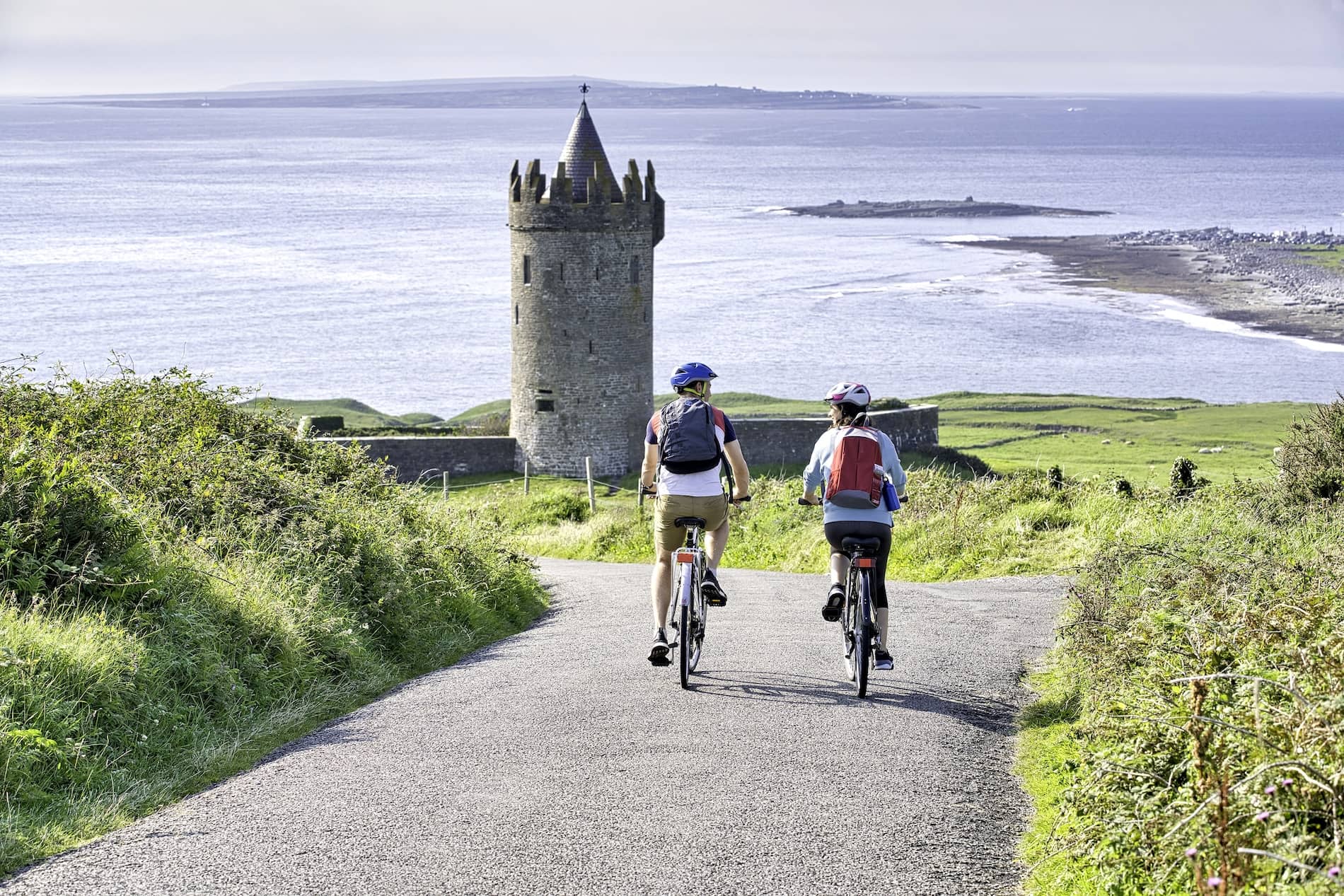 Deux cyclistes se dirigent vers le château de Doonagore dans le comté de Clare avec une vue imprenable sur l'océan Atlantique et la côte lointaine.