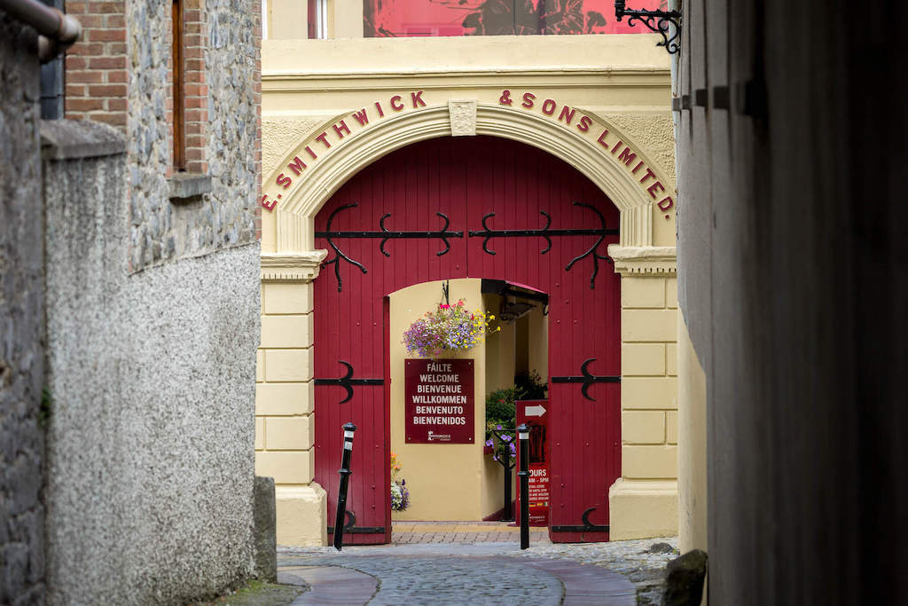 Entrance archway to the Smithwick’s Experience brewery tour with red doors and multilingual welcome sign.