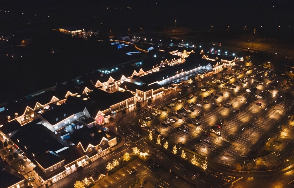 Aerial night view of Kildare Village outlet lit with festive lights, car park full of shoppers in County Kildare.