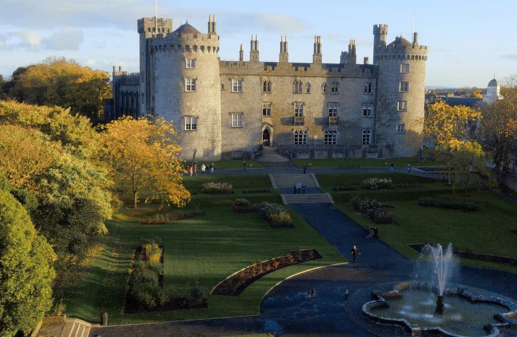 Historic Kilkenny Castle with manicured gardens, fountain and autumnal trees, viewed in soft afternoon light.