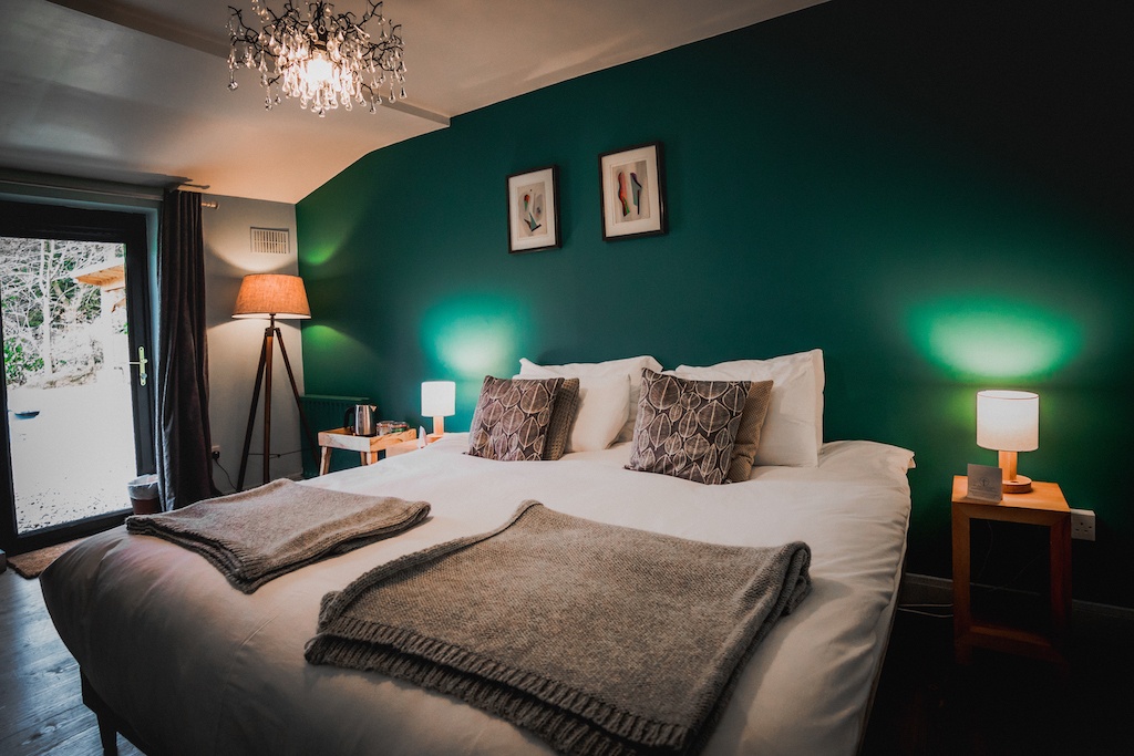 Cosy bedroom interior at Wicklow Escape with double bed, lamps and teal feature wall, creating a relaxing retreat.