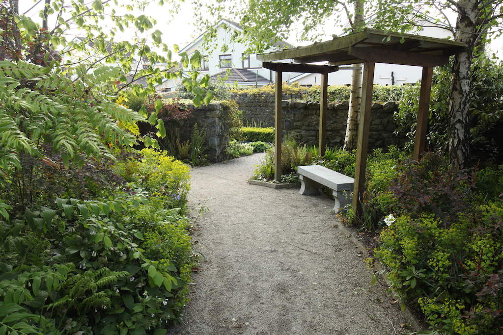 Shaded garden path with a stone bench and pergola surrounded by lush plants at Delta Sensory Gardens, Carlow.