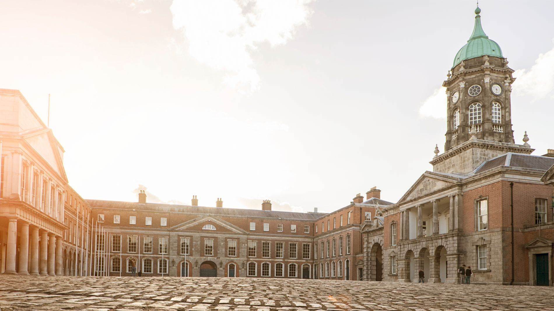 Een zonovergoten binnenplaats van Dublin Castle met zijn klokkentoren en historische stenen gebouwen.