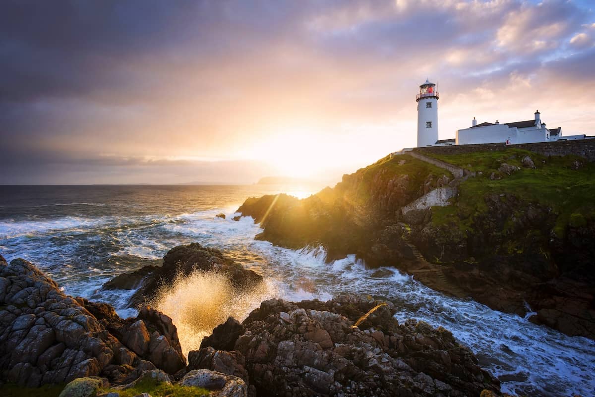 Sunset over Fanad Lighthouse in County Donegal, with waves crashing against the rugged Atlantic coast.