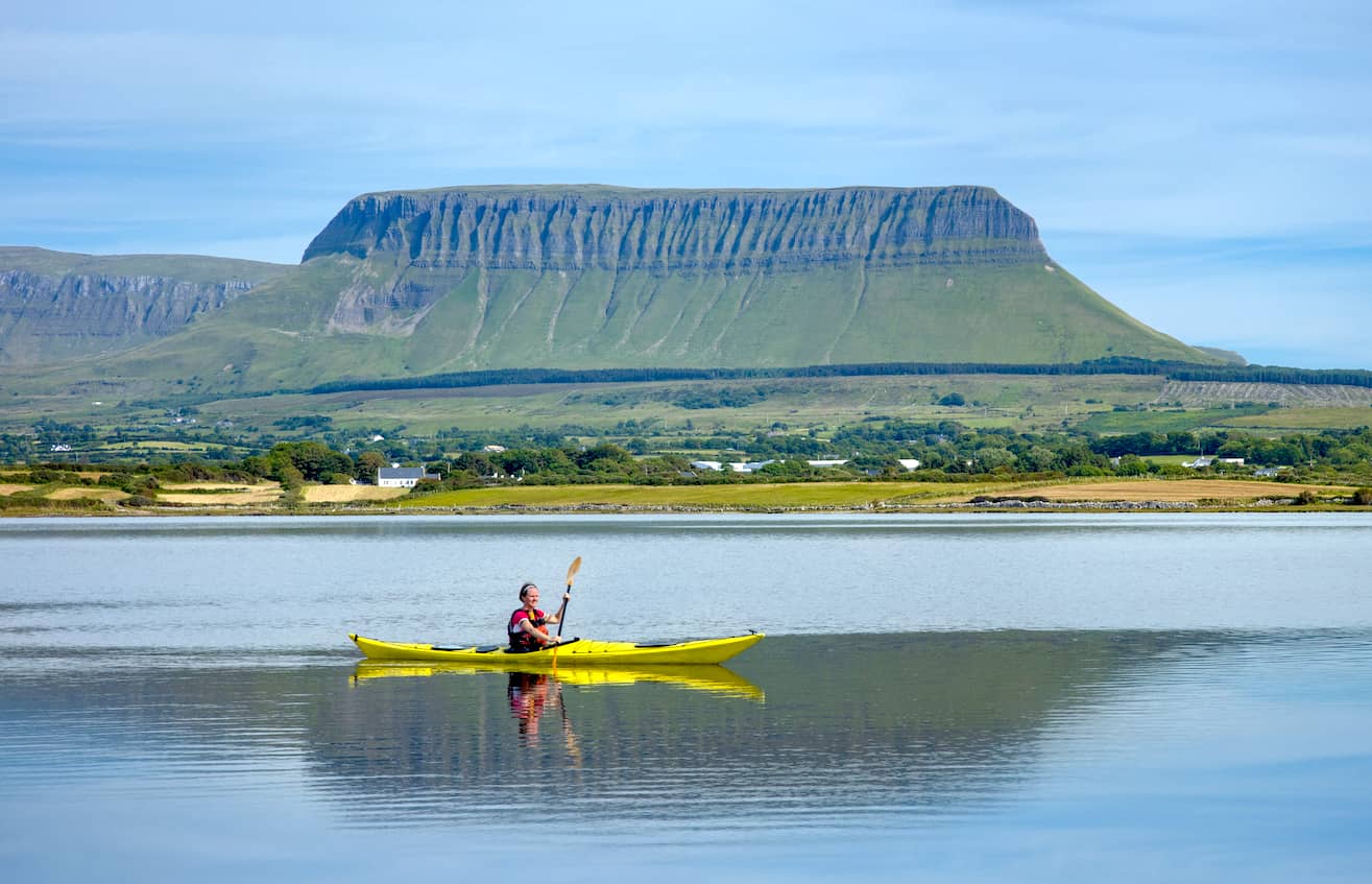 Kayaker paddling on calm water beneath the distinctive flat-topped Ben Bulben mountain in Sligo.