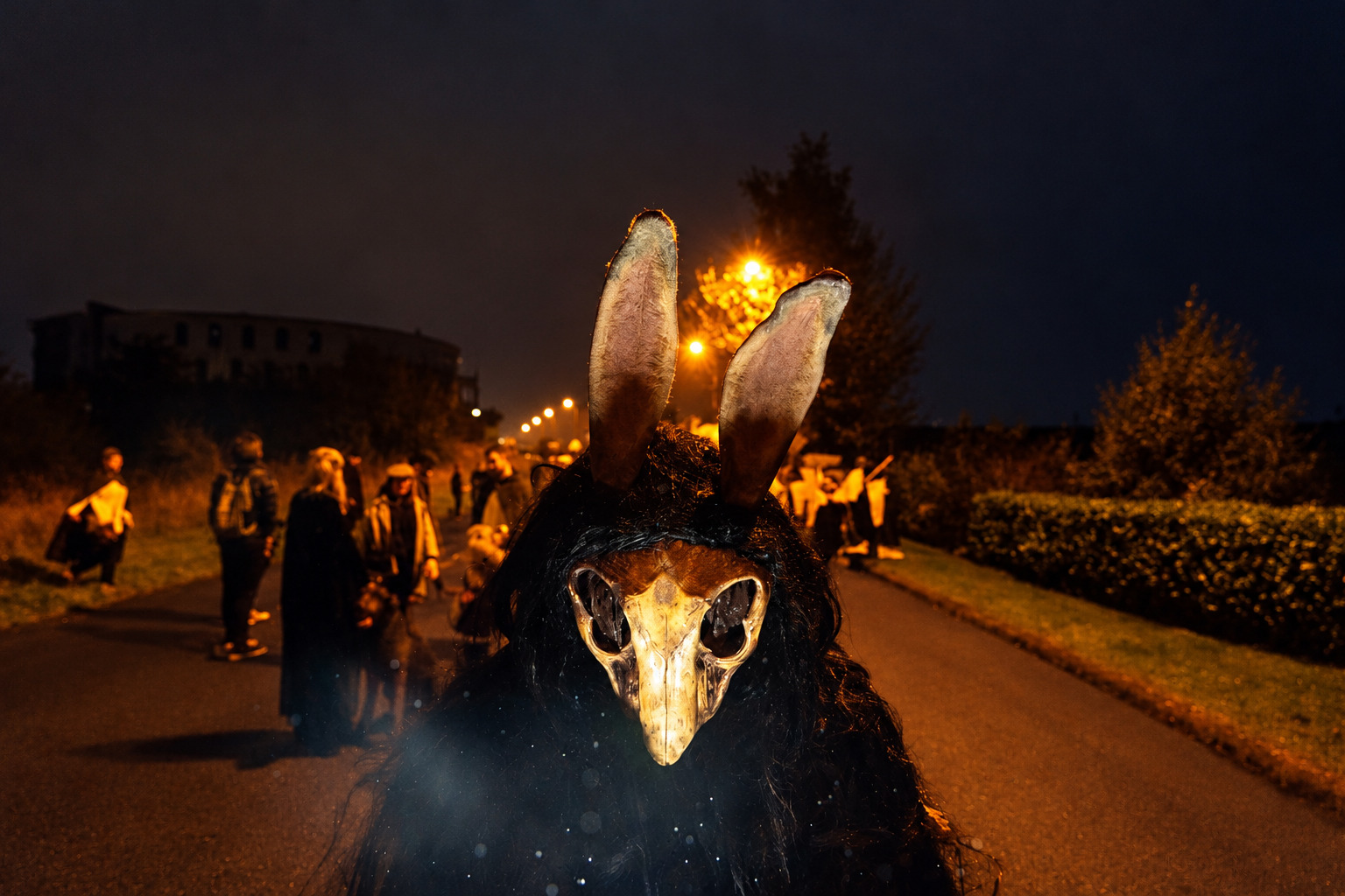 A costumed figure wearing a hare skull mask and tall ears leads a night-time procession at the Púca Festival in County Meath .